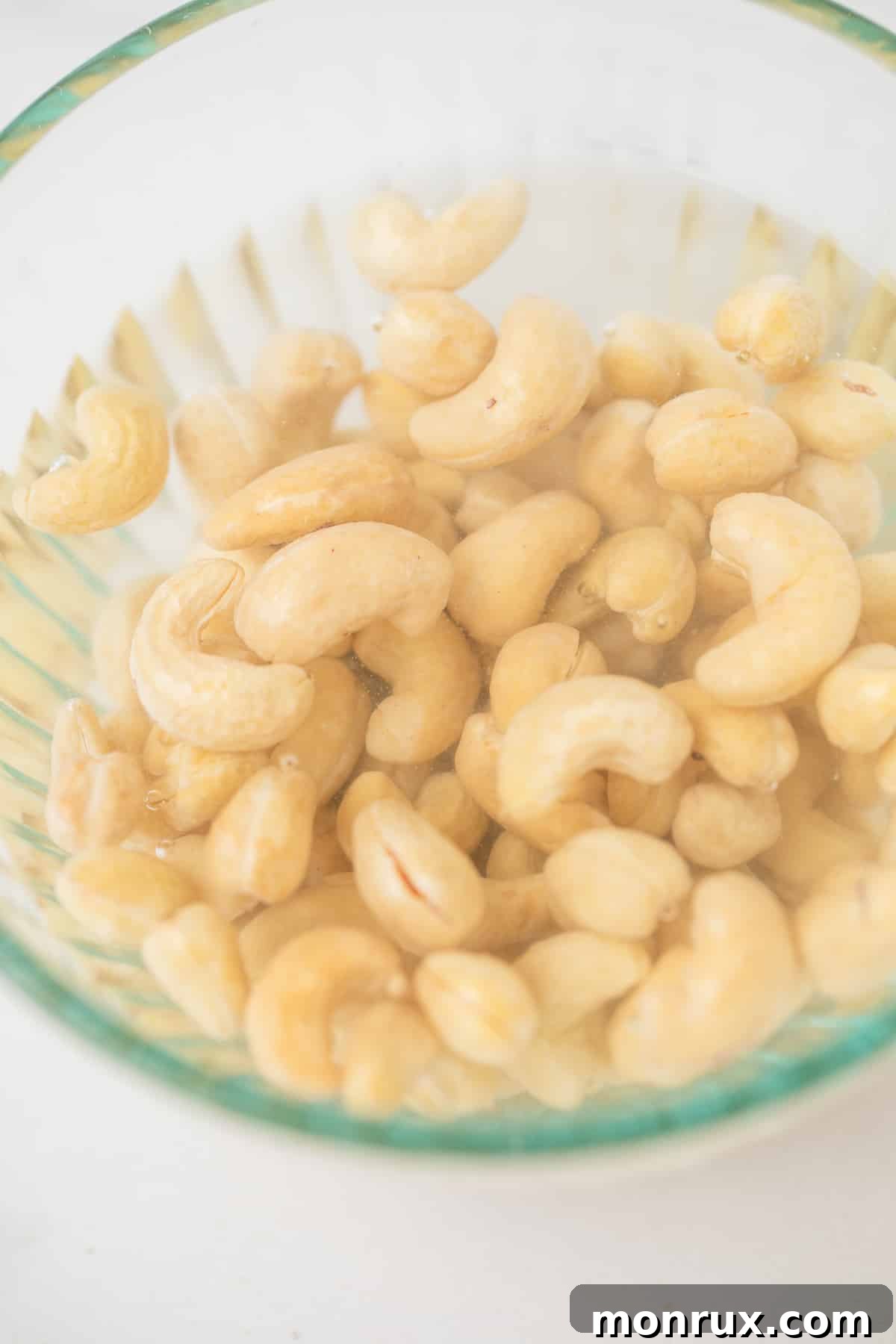 Raw cashews soaking in a bowl of hot water.