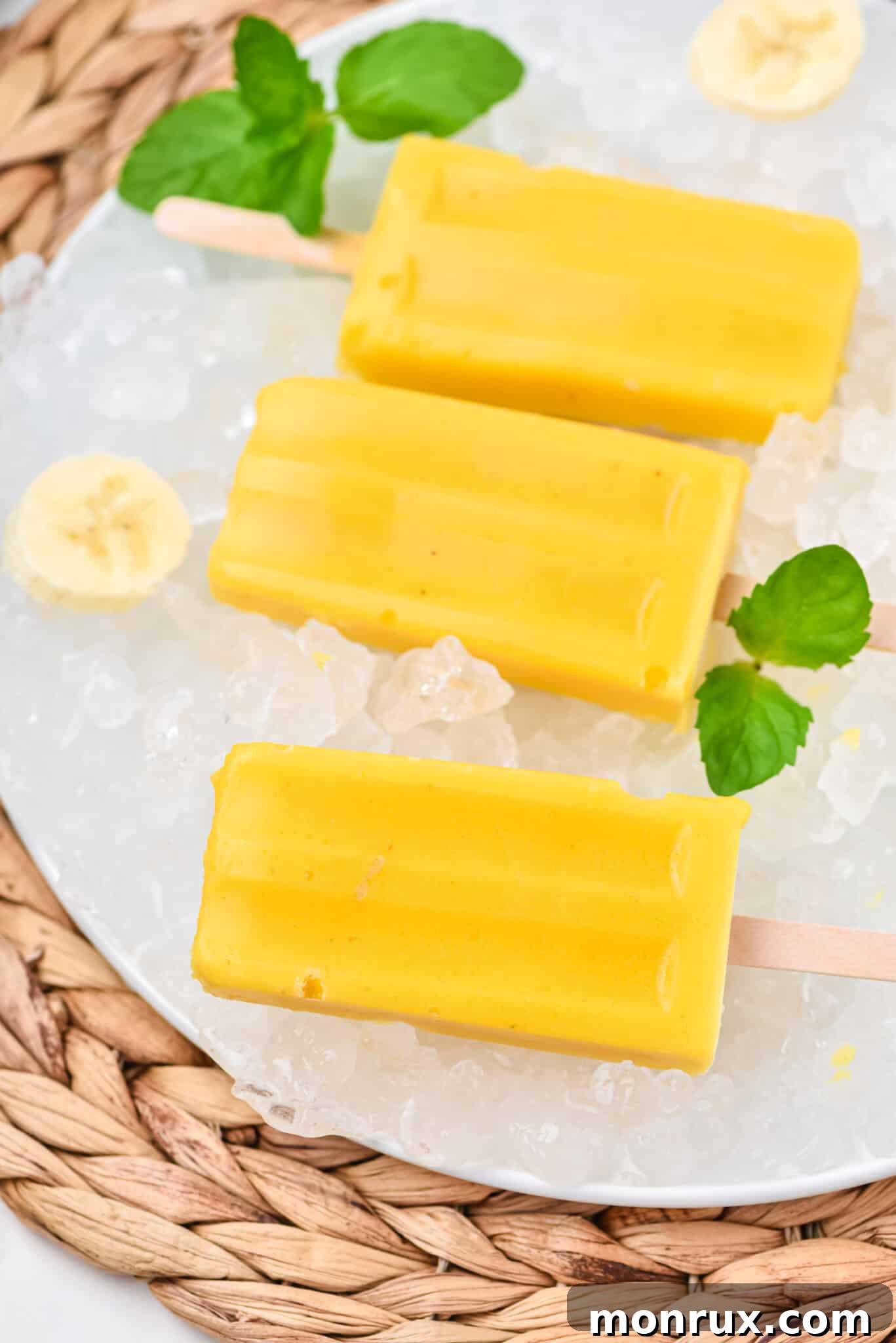 Bright yellow mango pineapple popsicles arranged on a bed of ice cubes, ready to be enjoyed.