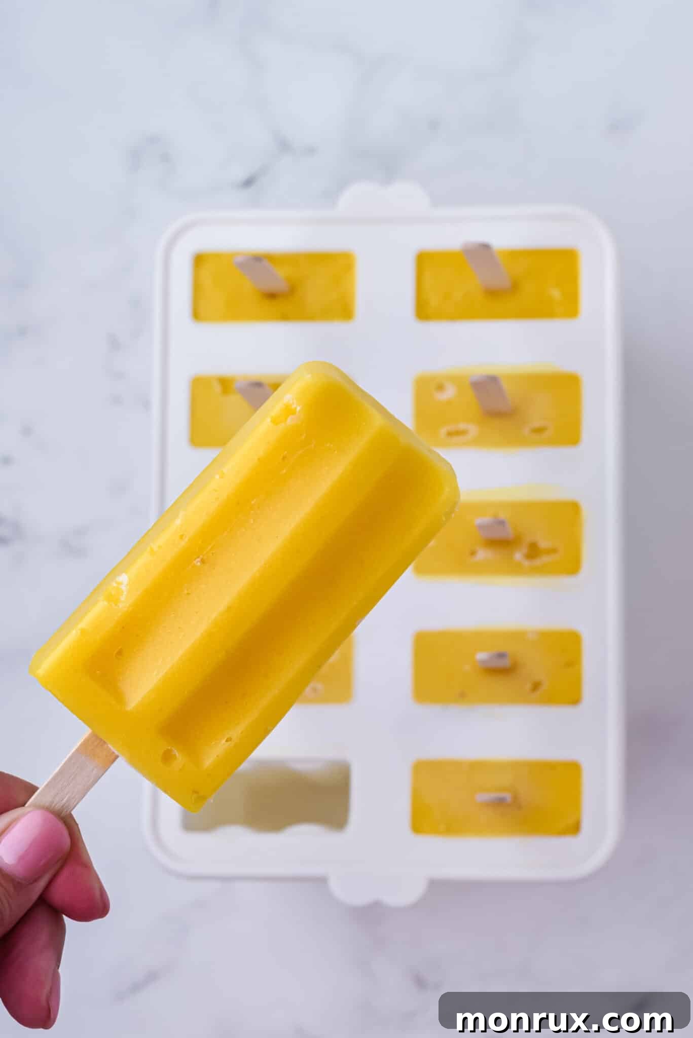 A hand gently removing a vibrant mango popsicle from its mold, highlighting its perfect texture.