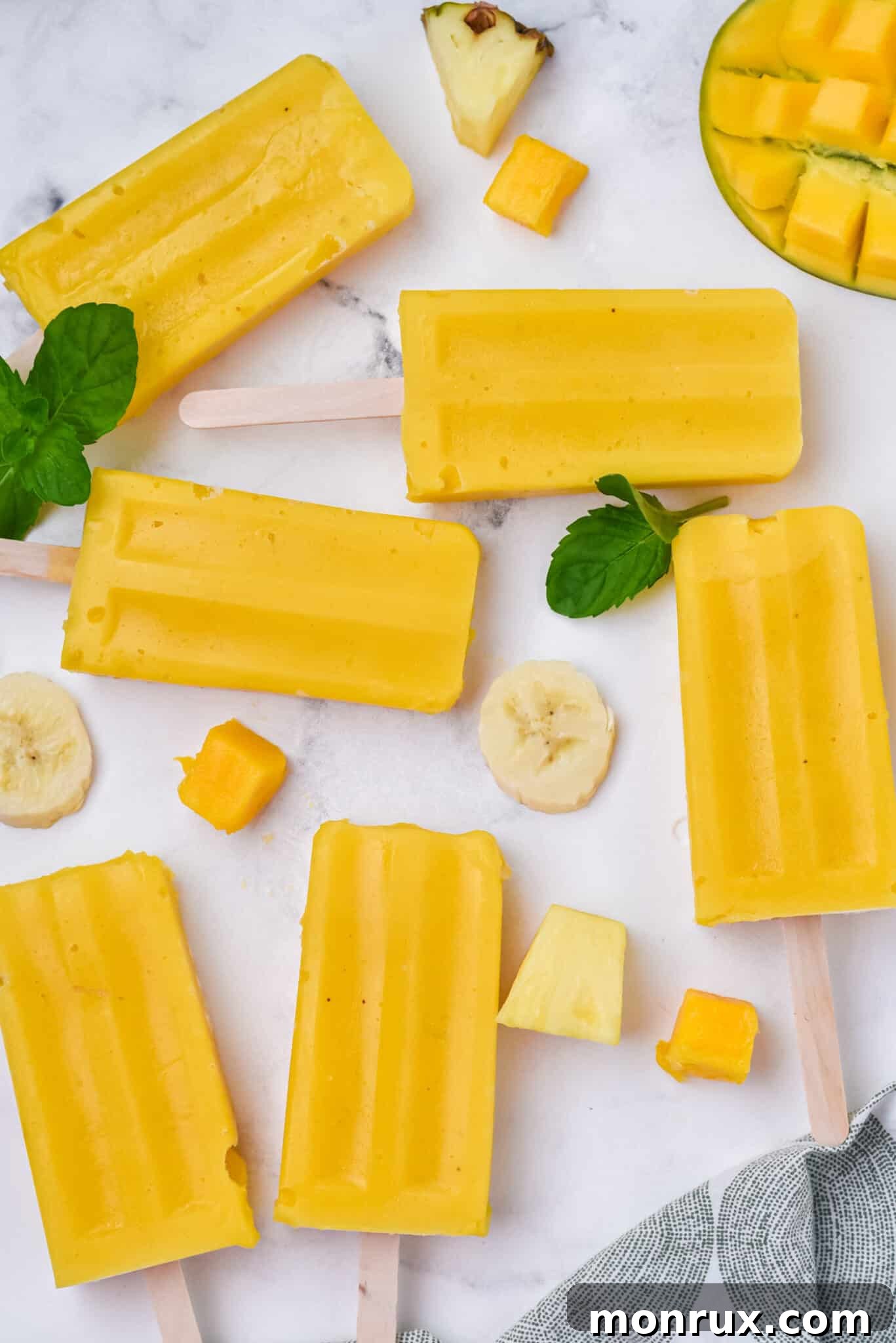 Multiple mango pineapple popsicles artfully arranged on a pristine white marble surface, showcasing their golden hue.