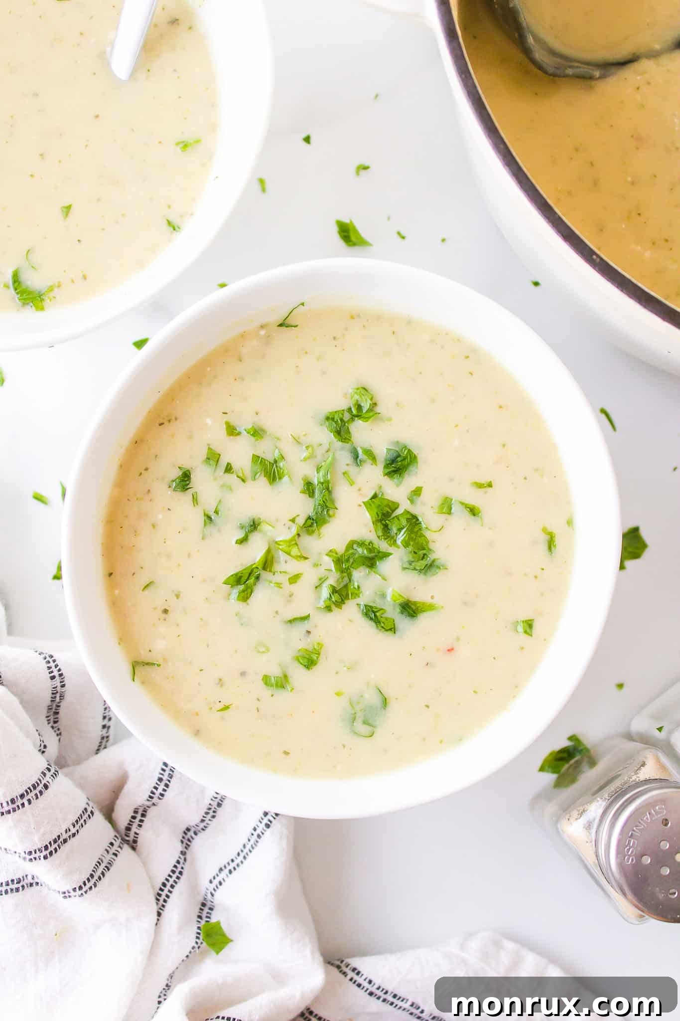 A small white bowl of zucchini potato soup, beautifully garnished with fresh parsley sprigs, ready to be served.