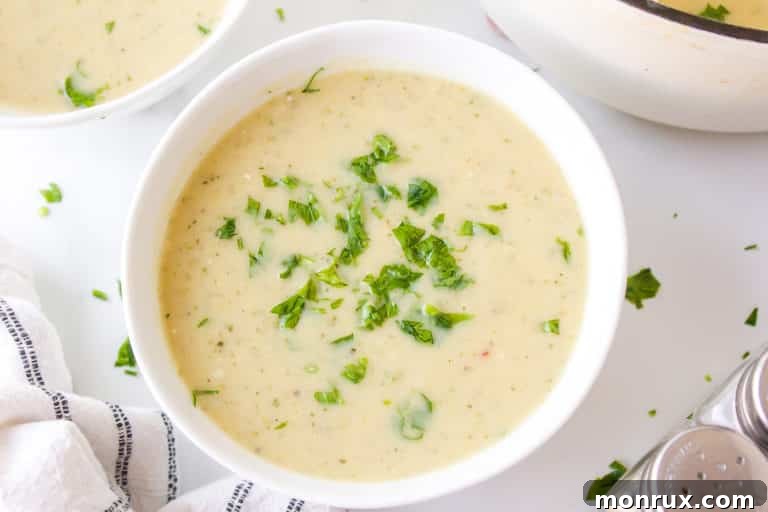 A small white bowl of zucchini potato soup garnished with parsley.