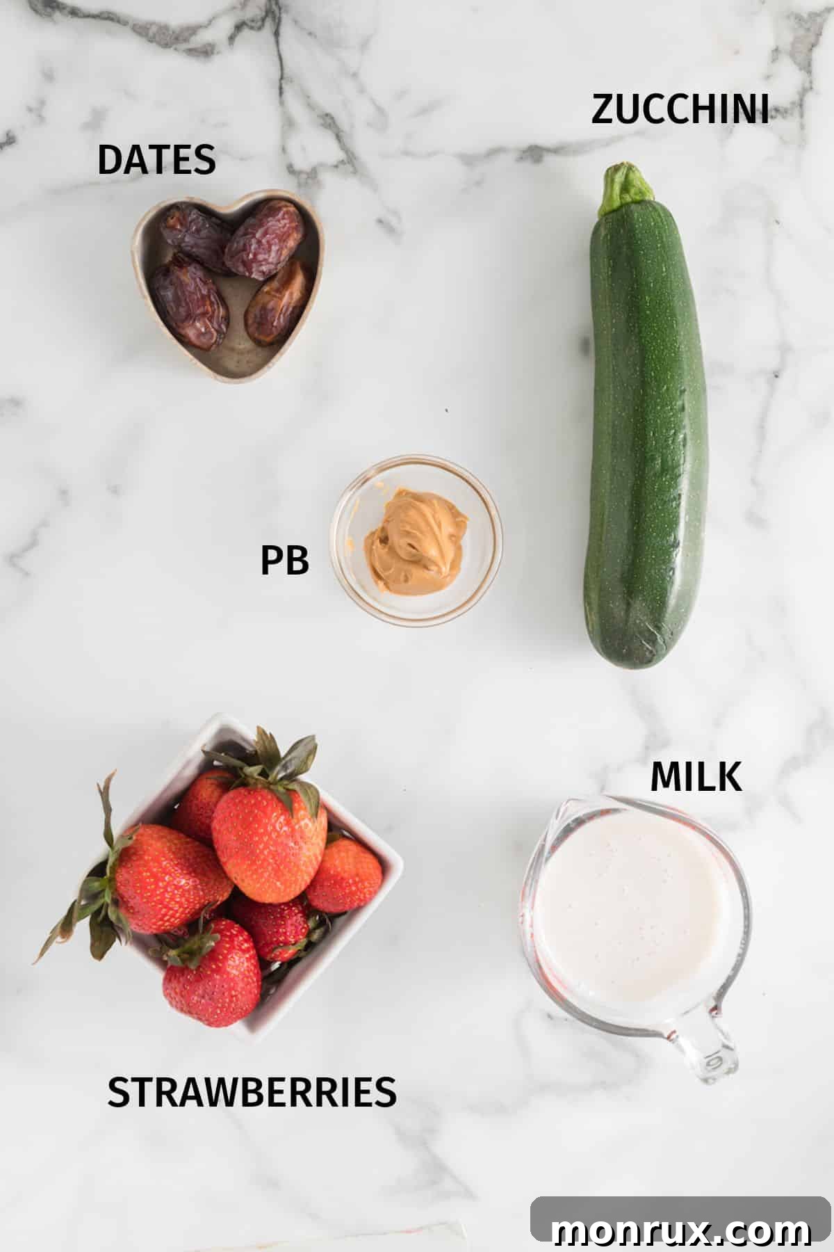 A flat lay image displaying the fresh ingredients required for a strawberry zucchini smoothie, neatly arranged on a white marble surface.