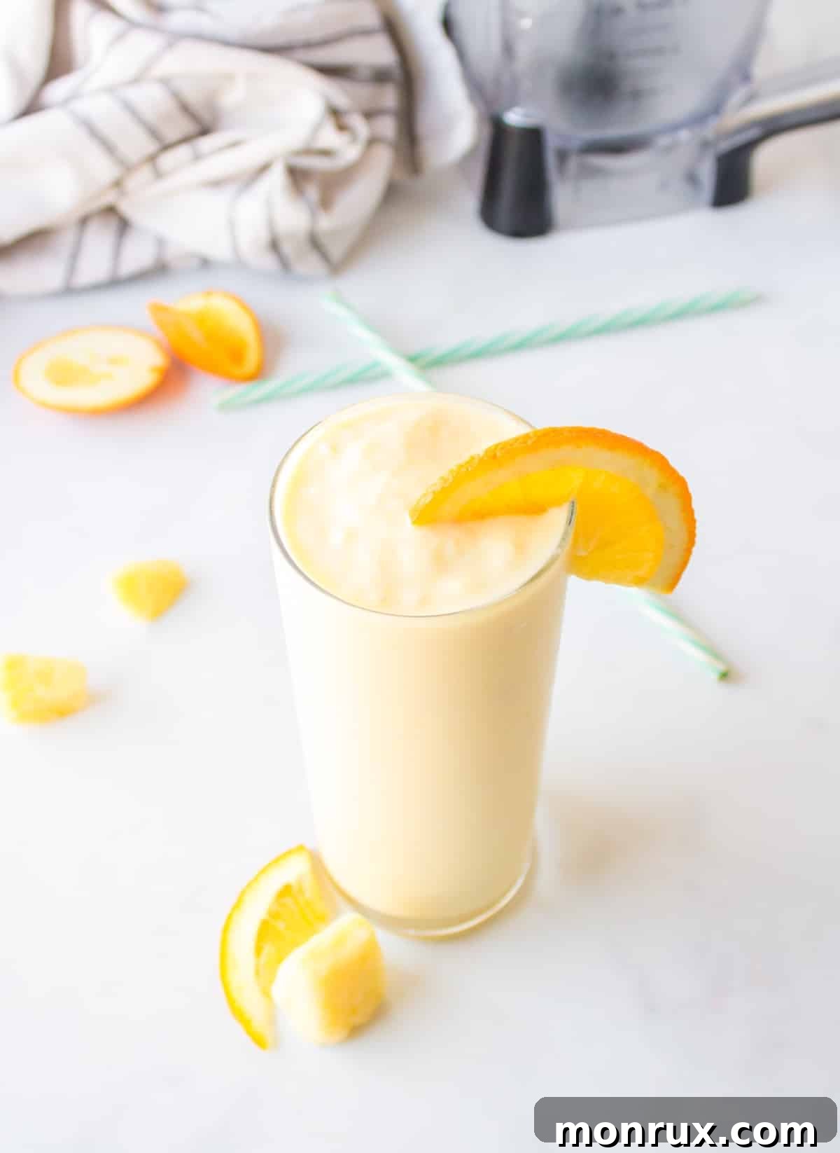 Vibrant Orange Pineapple Smoothie in a glass with a straw, garnished with fresh orange slices and pineapple.