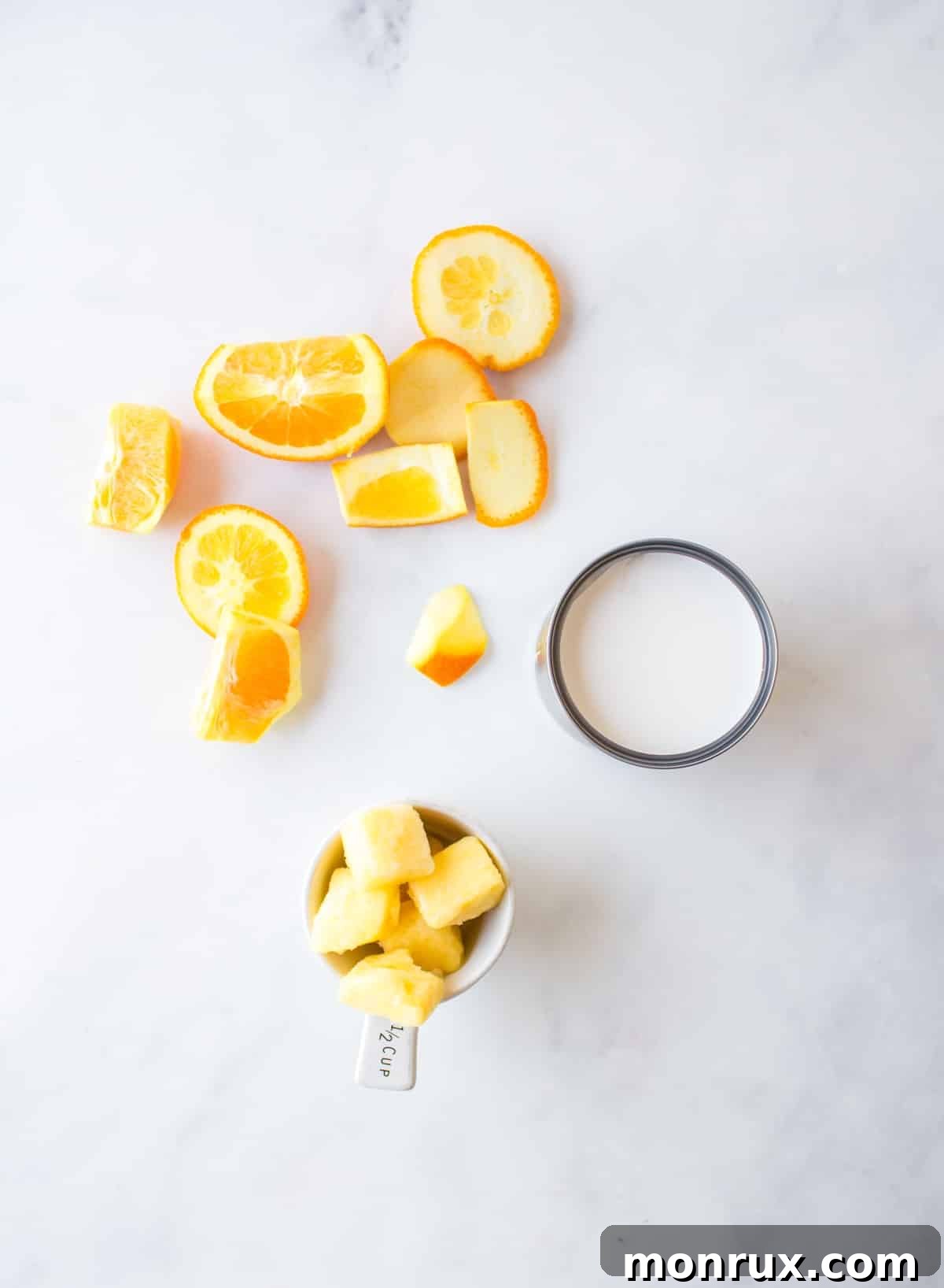 Fresh oranges, frozen pineapple chunks, and a can of coconut milk laid out as ingredients for a smoothie.