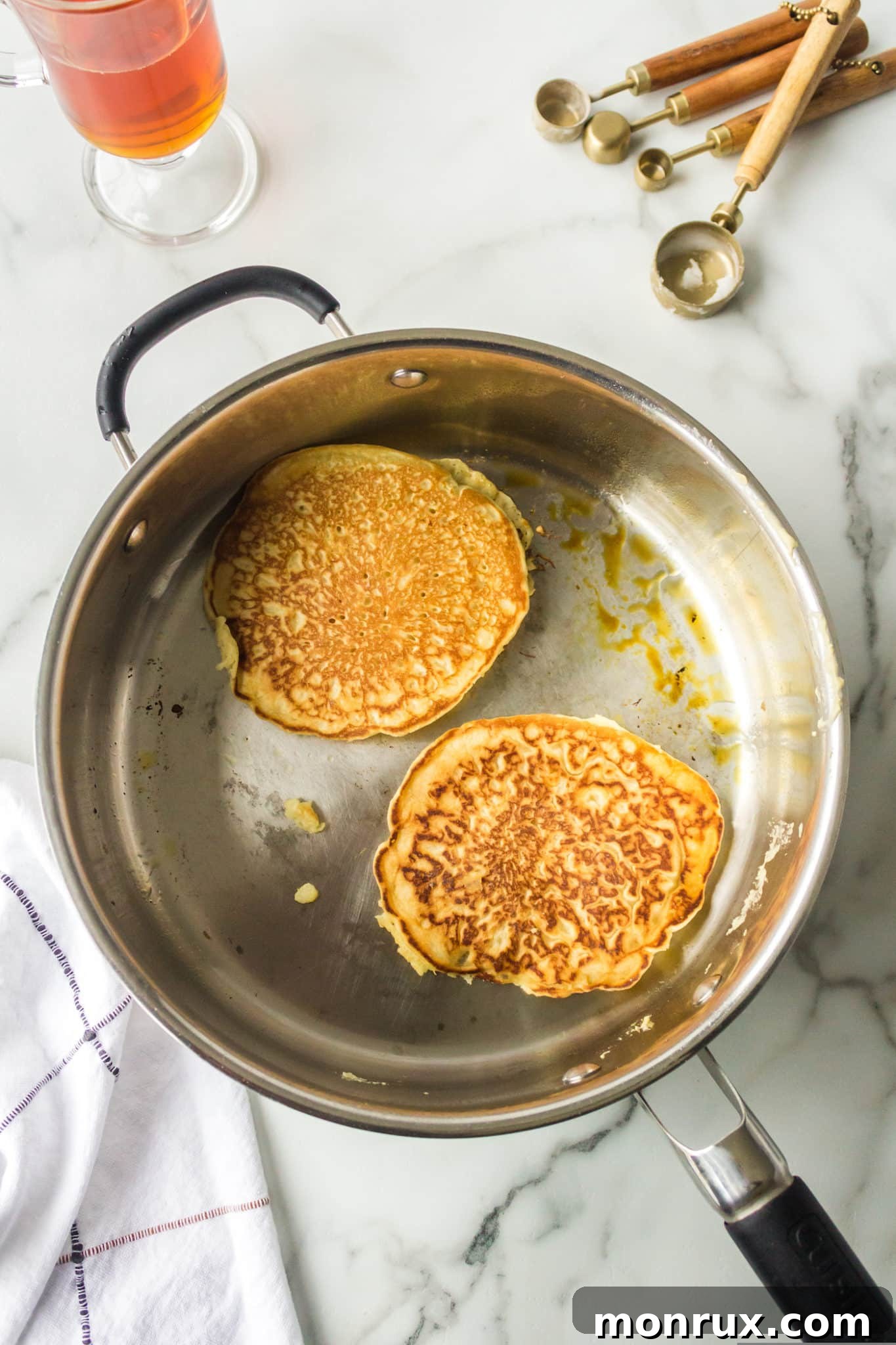 Two golden brown rice flour pancakes cooking in a skillet.
