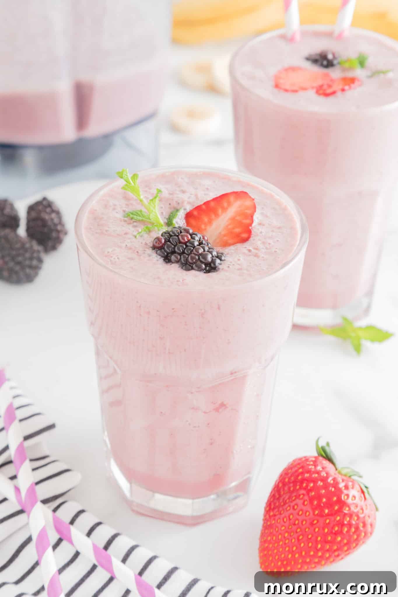 A tall glass of strawberry blackberry banana smoothie topped with fresh berries and a straw, showcasing its rich purple and red hues.