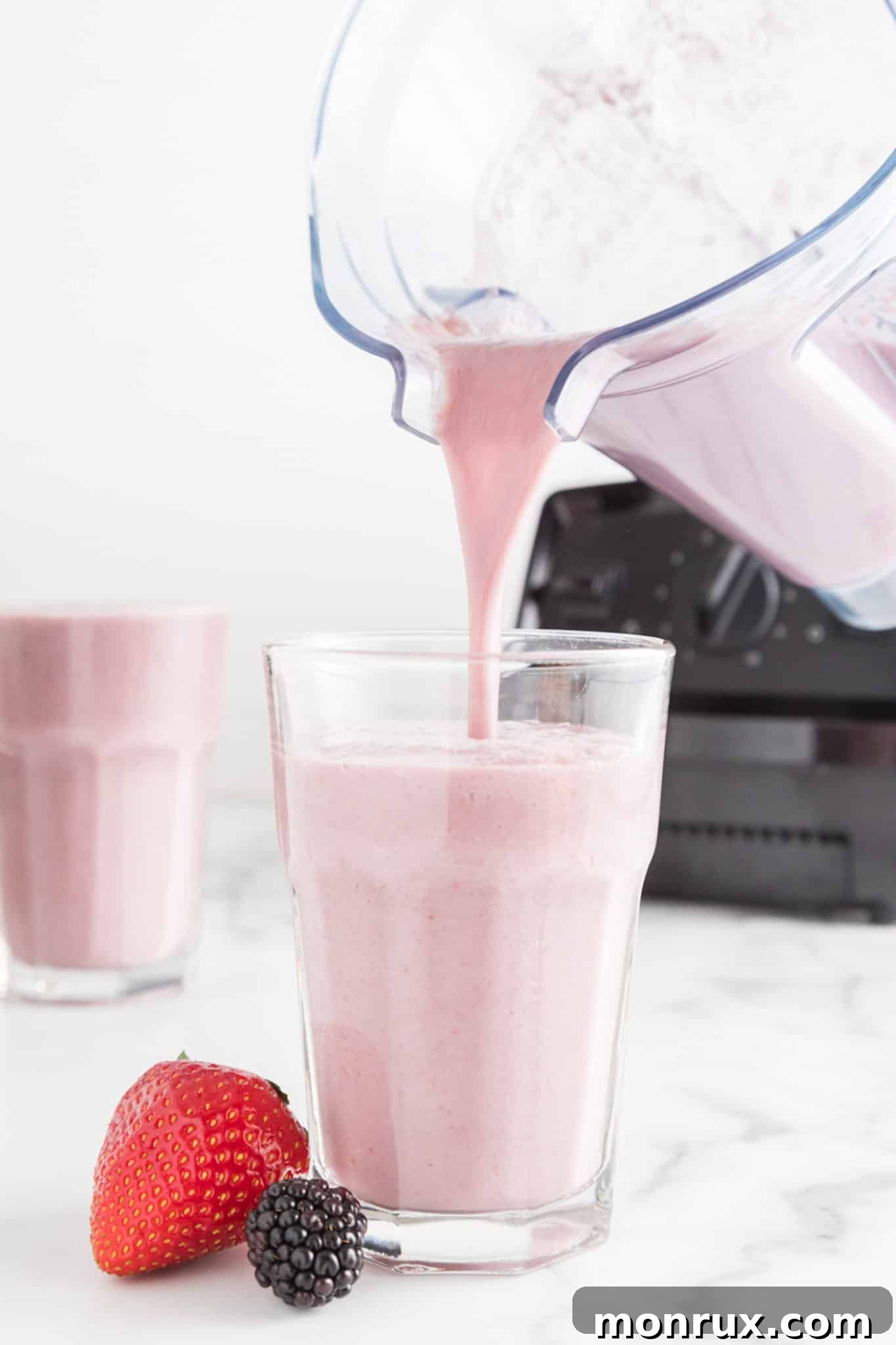 A blender pouring a vibrant strawberry blackberry banana smoothie into a tall glass, ready to be enjoyed.