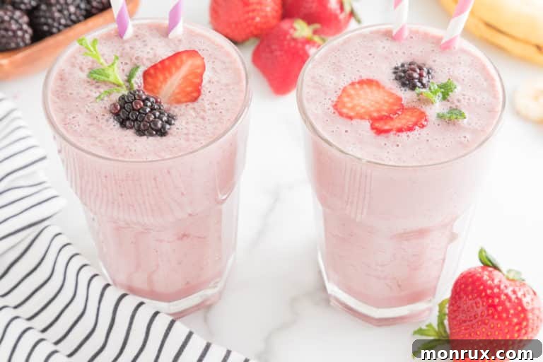 Two glasses of strawberry blackberry banana smoothie with fresh fruit and paper straws.
