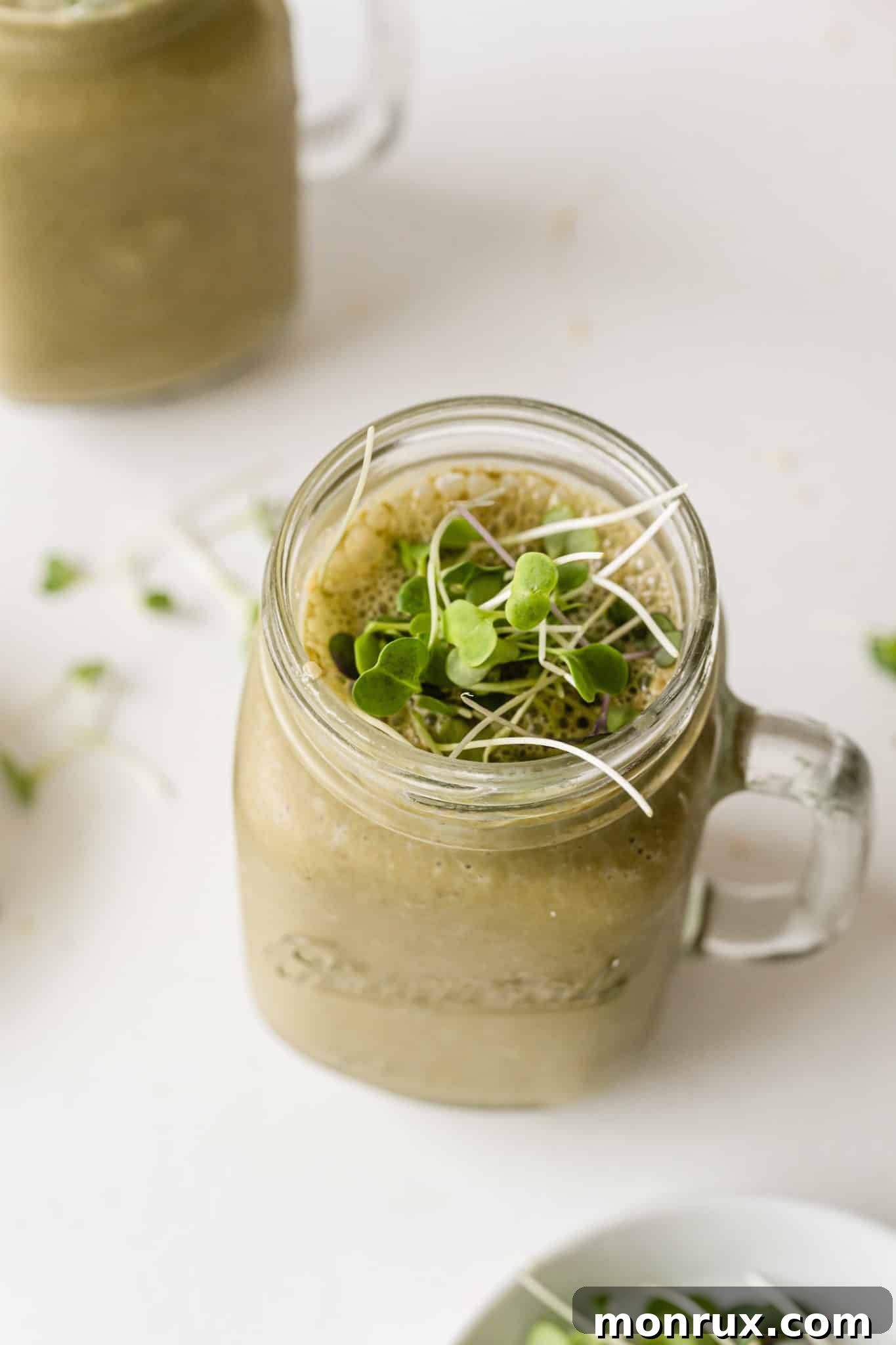A vibrant green broccoli sprout smoothie, topped with a small handful of fresh broccoli sprouts, served in a glass on a table.