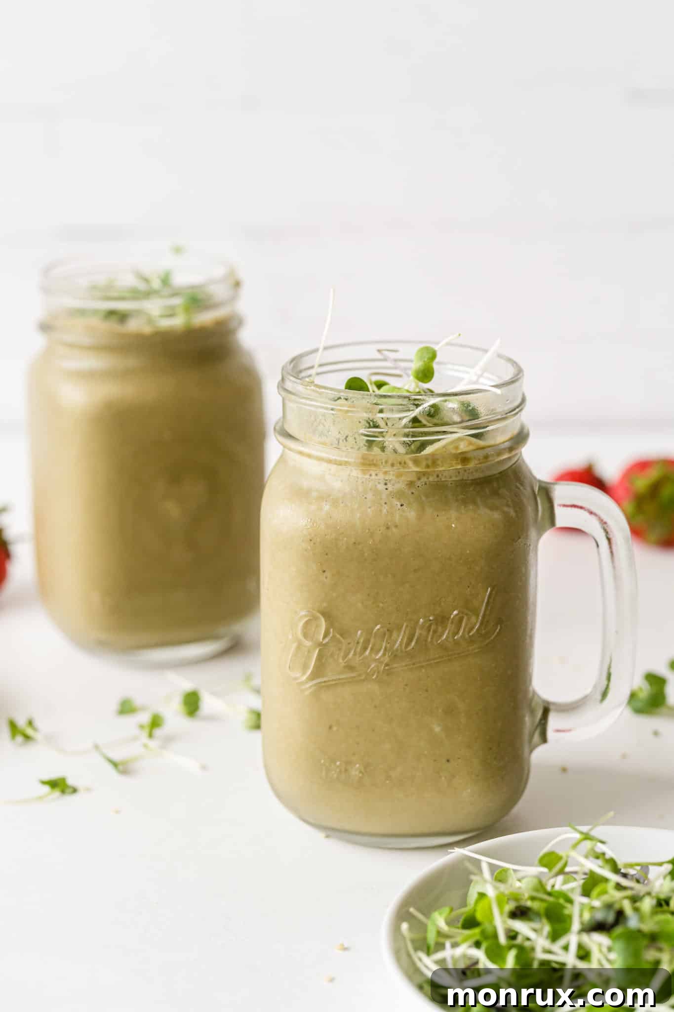 Two glasses of vibrant green broccoli sprout smoothie, garnished with fresh sprouts, on a wooden table, with more fresh sprouts scattered around.