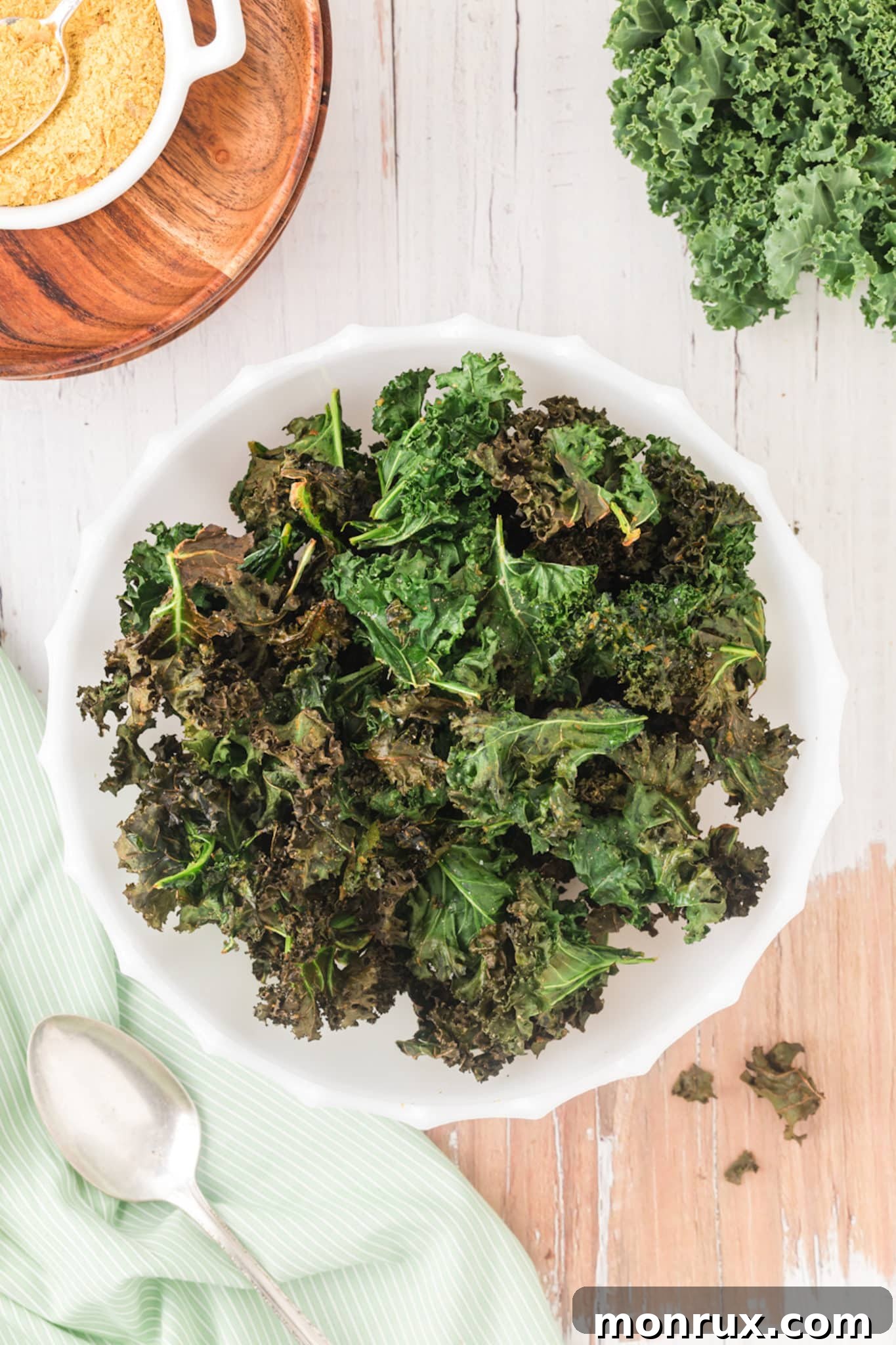 A bowl of freshly made air fryer kale chips, generously sprinkled with nutritional yeast for a cheesy flavor, sits invitingly on a wooden table.