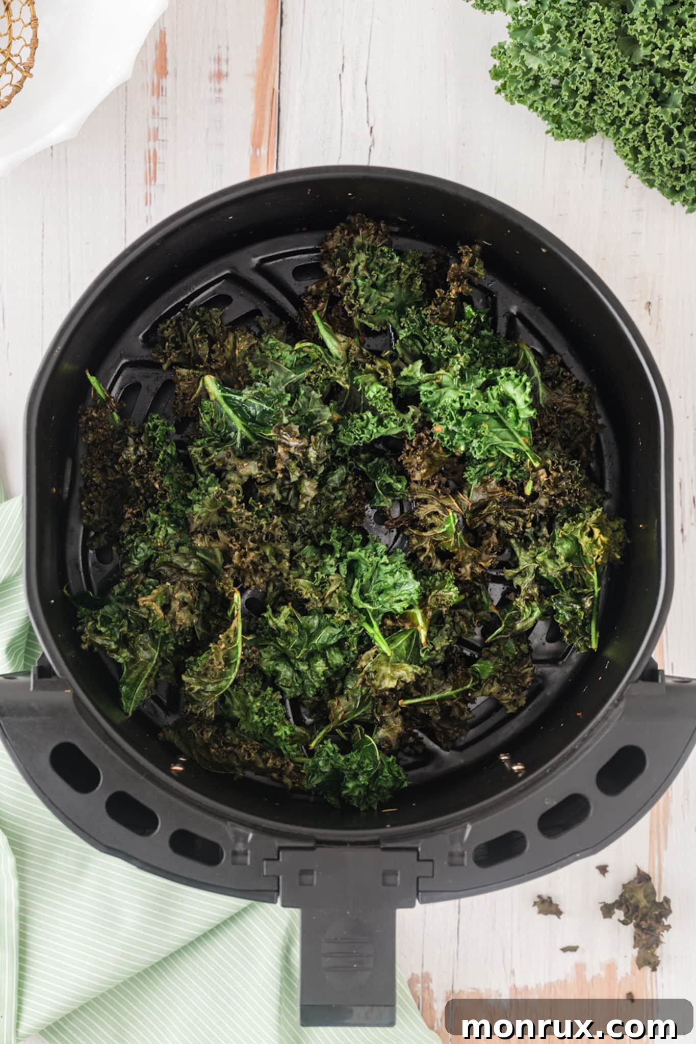 A close-up shot of perfectly cooked and crispy kale chips inside an air fryer basket, showing their golden-brown texture.