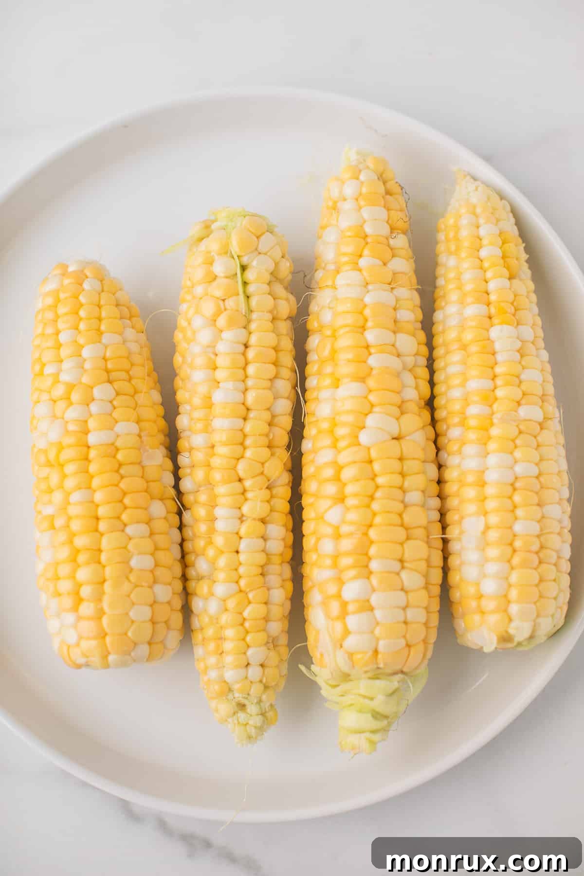 four pieces of corn on a plate with the corn husks removed.