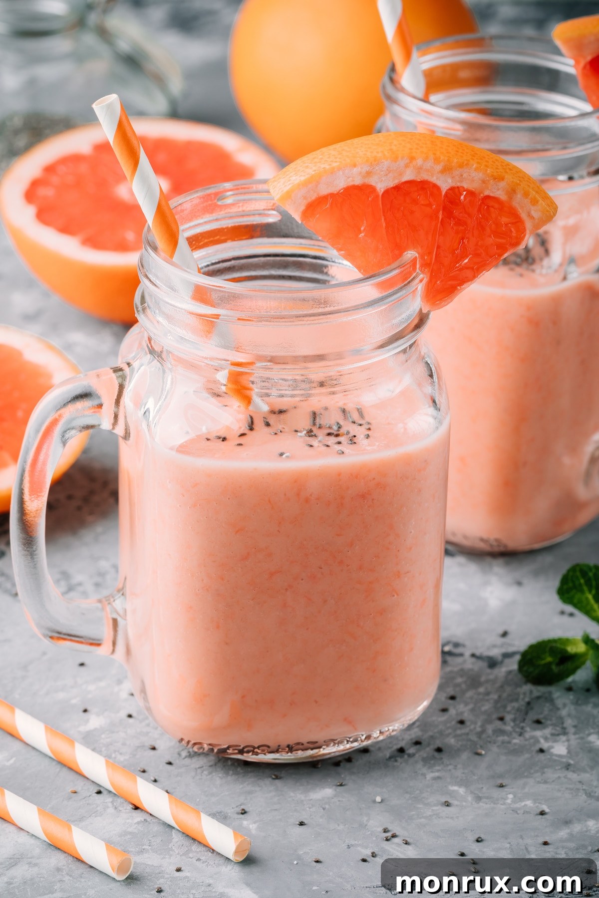 Two glasses of beautifully pink grapefruit smoothie, garnished with a grapefruit slice, placed on a rustic wooden table.