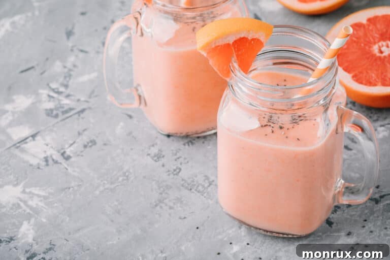 Two glasses of grapefruit smoothie with a grapefruit slice garnish on a table, ready to be served.