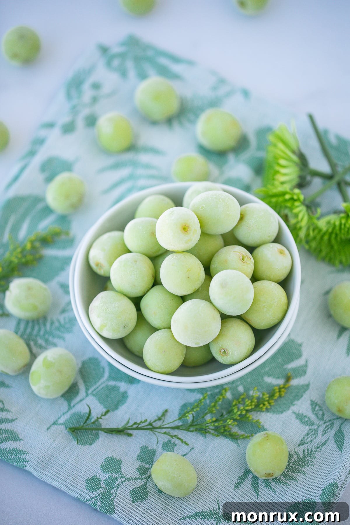 A vibrant bowl of green frozen grapes, glistening with frost, sits invitingly on a clean kitchen countertop.