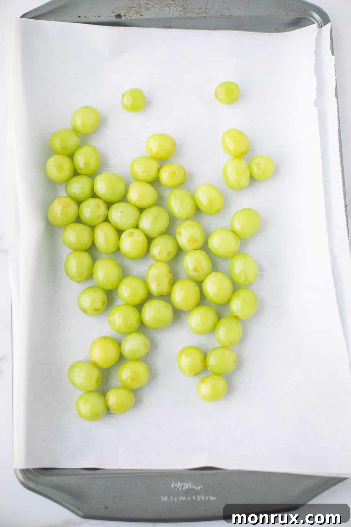 Freshly washed grapes are carefully laid out in a single layer on a baking sheet lined with parchment paper, stems removed.