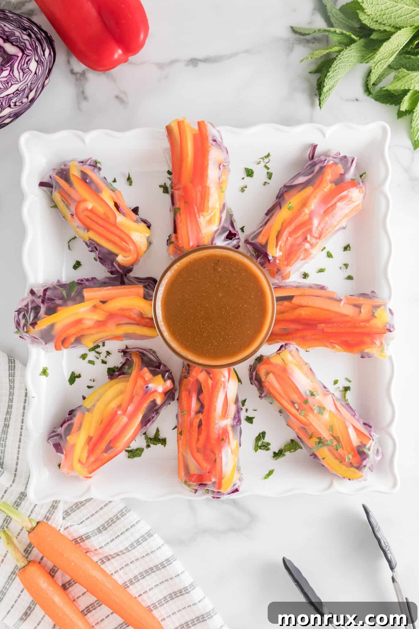 Freshly prepared vegan summer rolls neatly arranged on a plate, with a small bowl of creamy peanut dipping sauce beside them.