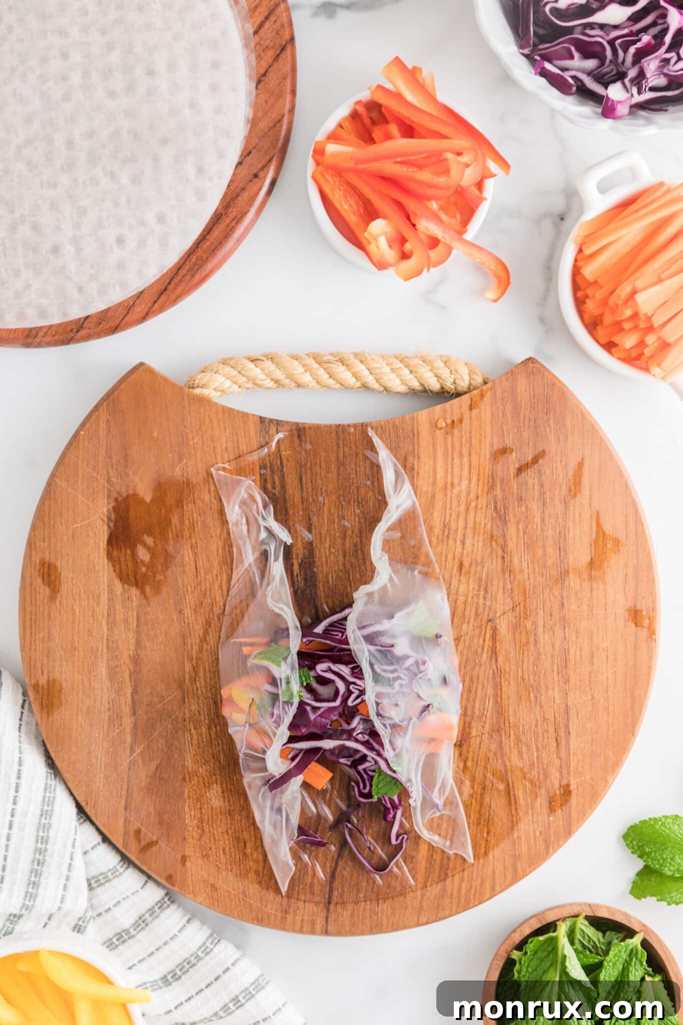Hands carefully placing colorful vegetable strips onto a softened rice paper wrapper laid on a clean surface.