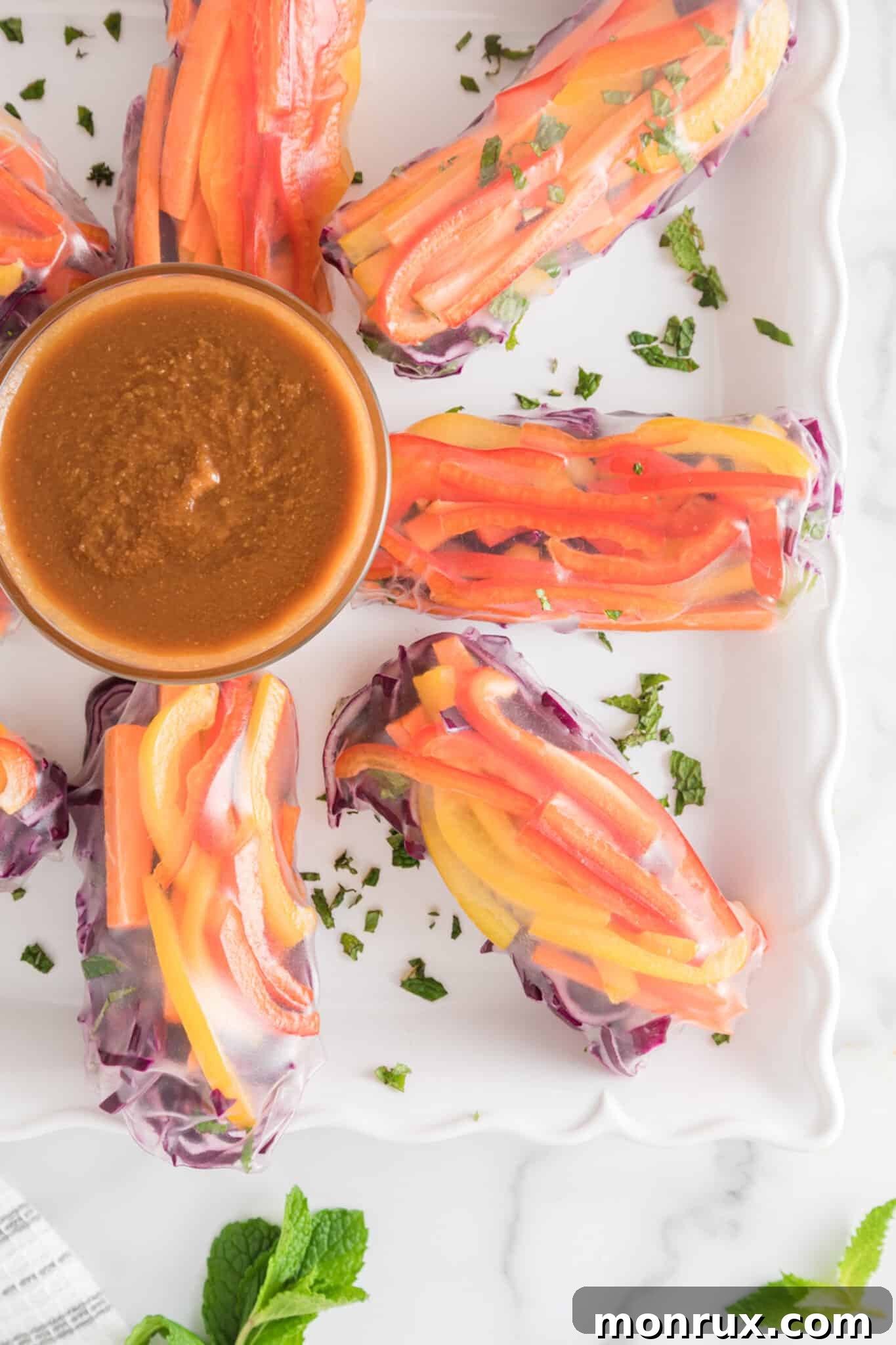 A plate brimming with freshly made vegan summer rolls, served alongside a small bowl of rich peanut sauce, ready to be enjoyed.