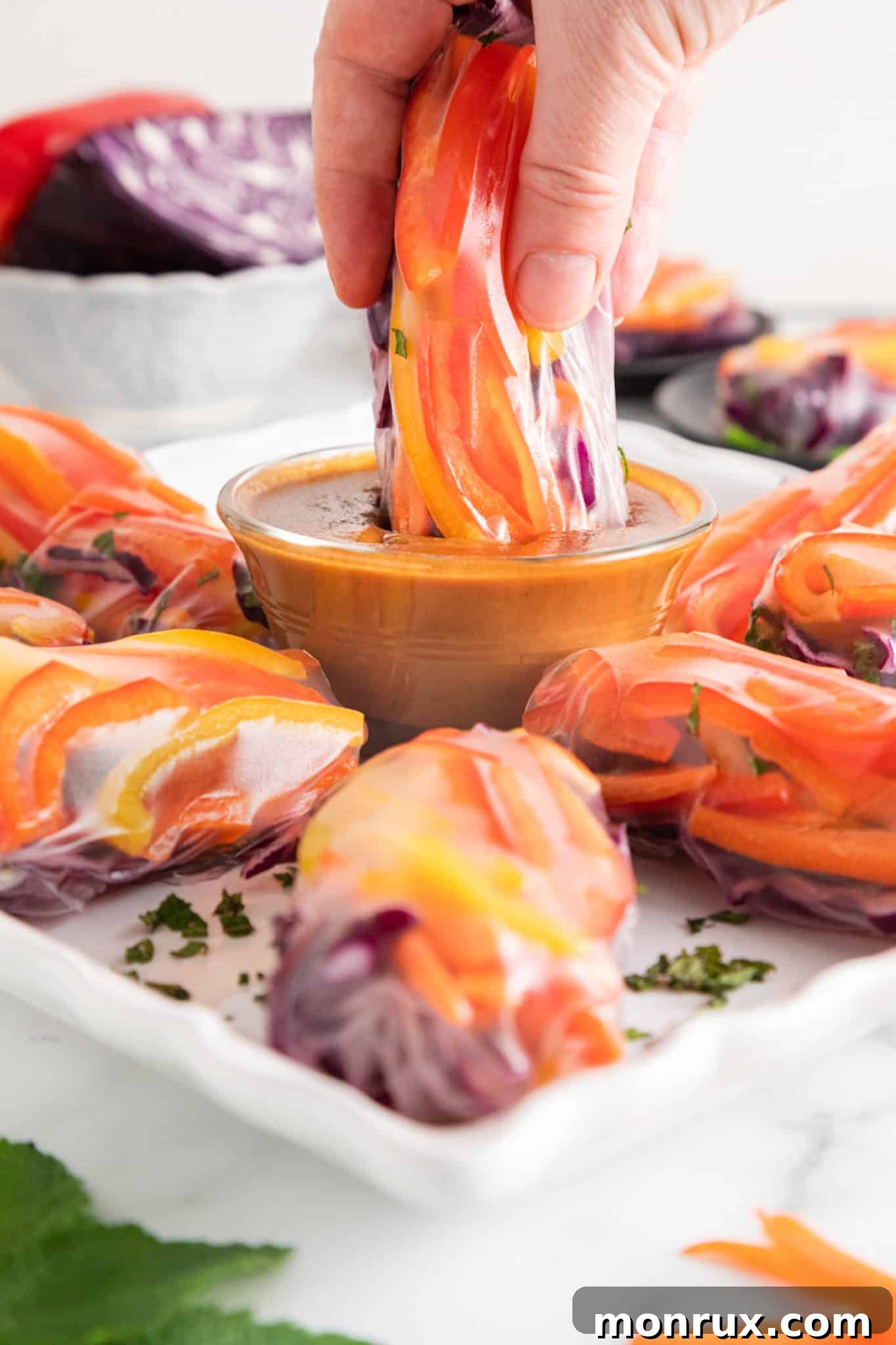 A vegan summer roll is elegantly dipped into a bowl of rich, creamy peanut sauce, showcasing its delicious appeal.