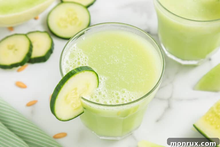A small glass filled with Honeydew Cucumber Smoothie with a cucumber slice on the rim, a mint leaf, and a straw.