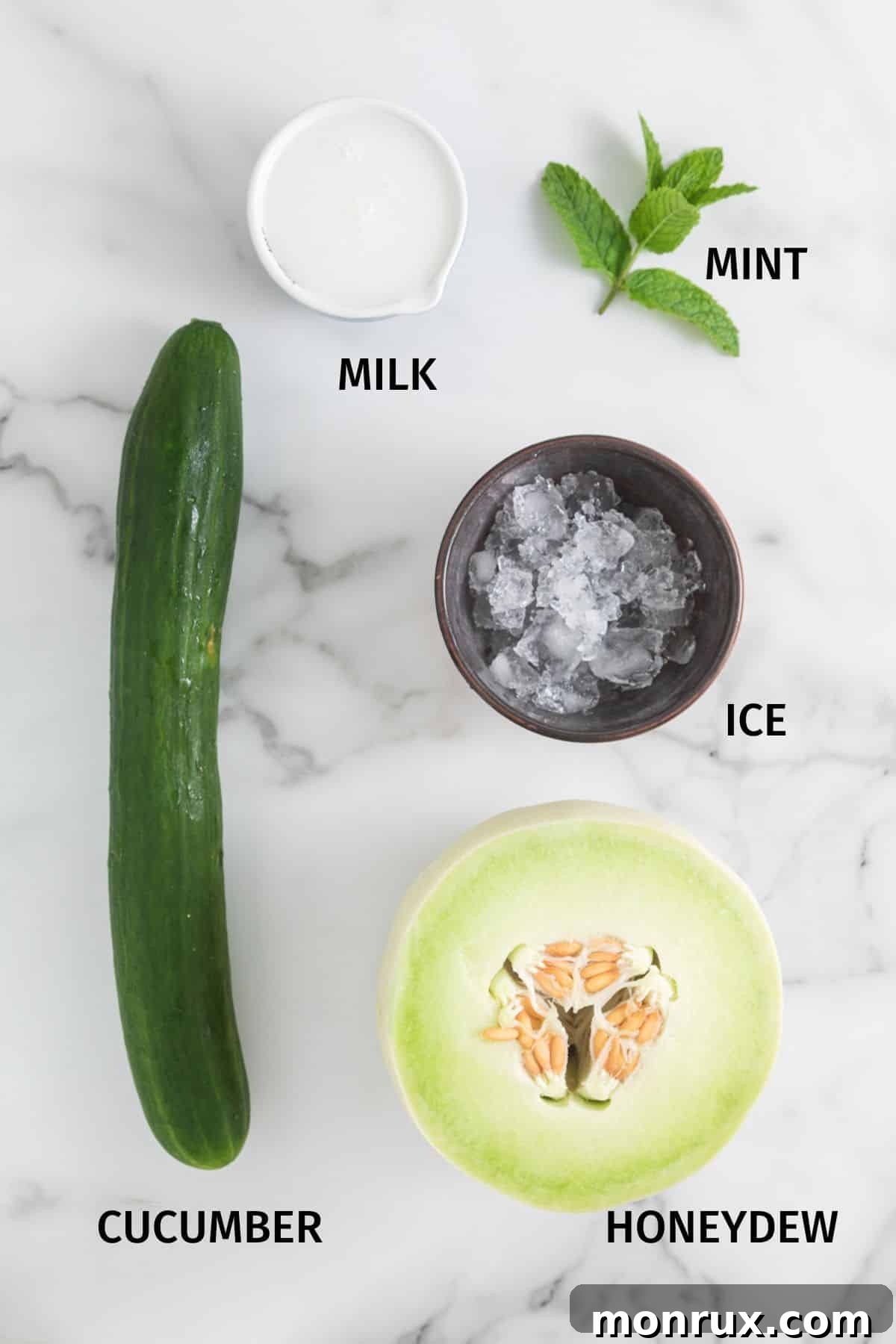 Fresh honeydew melon, cucumber, a carton of coconut milk, and fresh mint leaves laid out on a white surface, ready for blending.