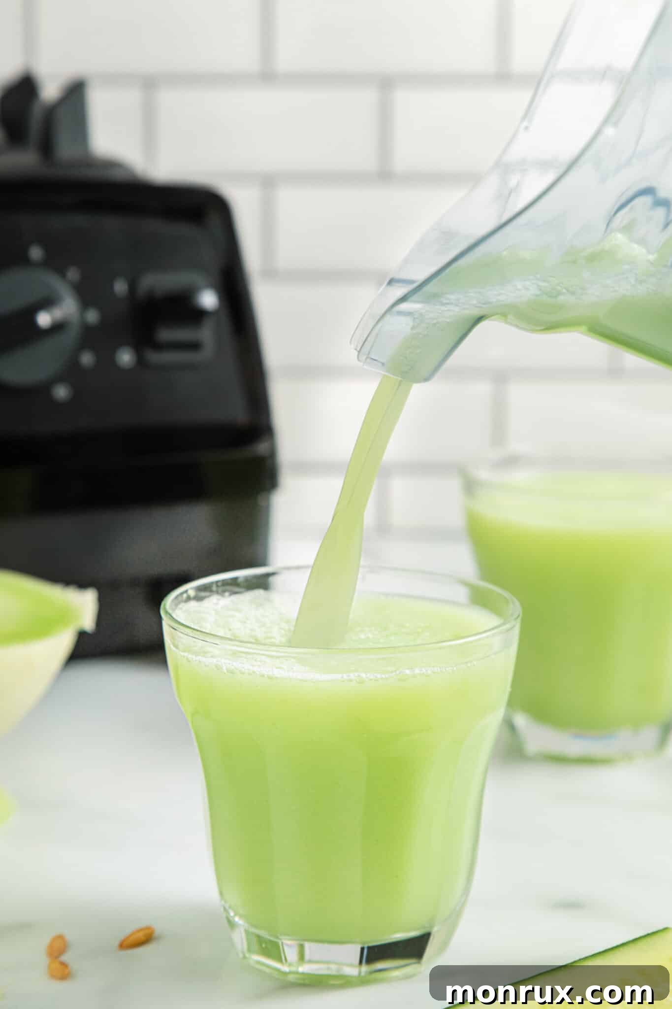 A stream of vibrant green honeydew cucumber smoothie being poured from a blender into a clear glass, showing its smooth texture.