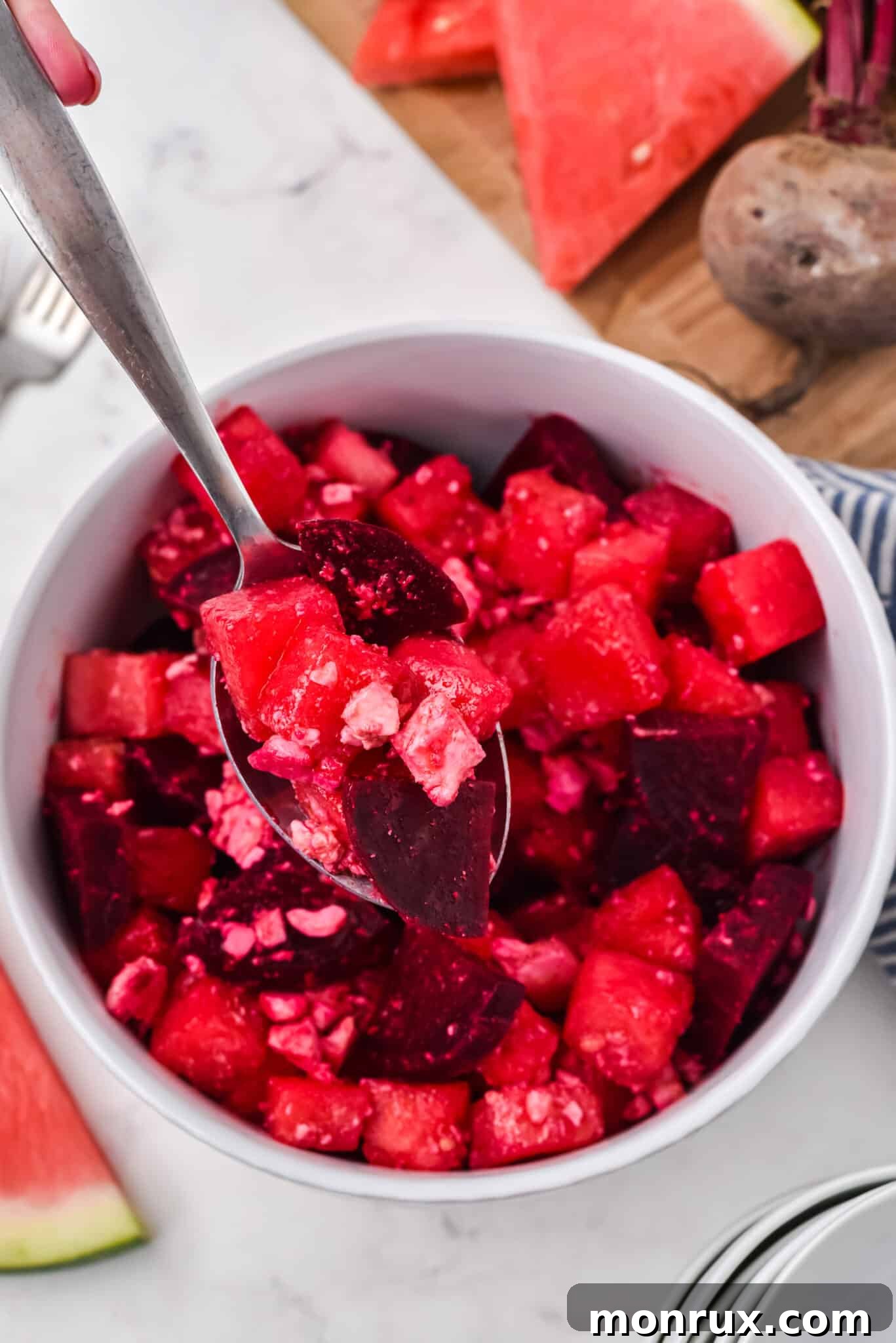 A spoon holding a vibrant Watermelon Beet Salad over a small white bowl, showcasing the fresh ingredients. This light, refreshing, and flavorful salad is perfect for summer gatherings, cookouts, or a healthy meal, and is vegetarian, gluten-free, with a vegan option.