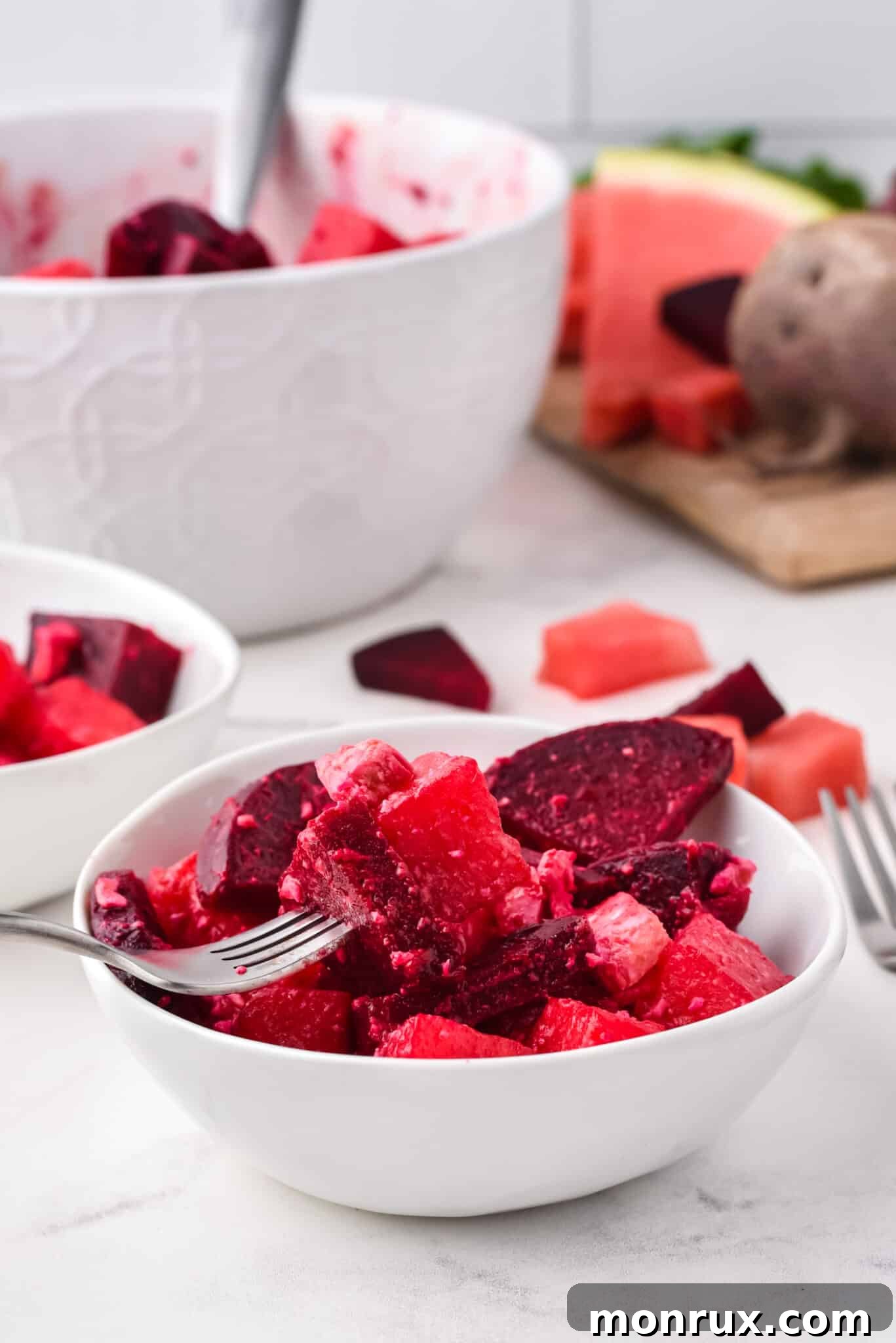A fork holding a bite of Watermelon Beet Salad over a small white bowl, ready to be enjoyed. This light, refreshing, and flavorful salad is perfect for summer gatherings, cookouts, or a healthy meal, and is vegetarian, gluten-free, with a vegan option.