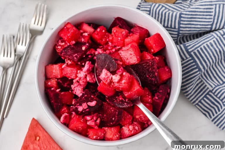A spoon holding a bit of watermelon beet salad over a small white bowl, illustrating the colorful and fresh ingredients.