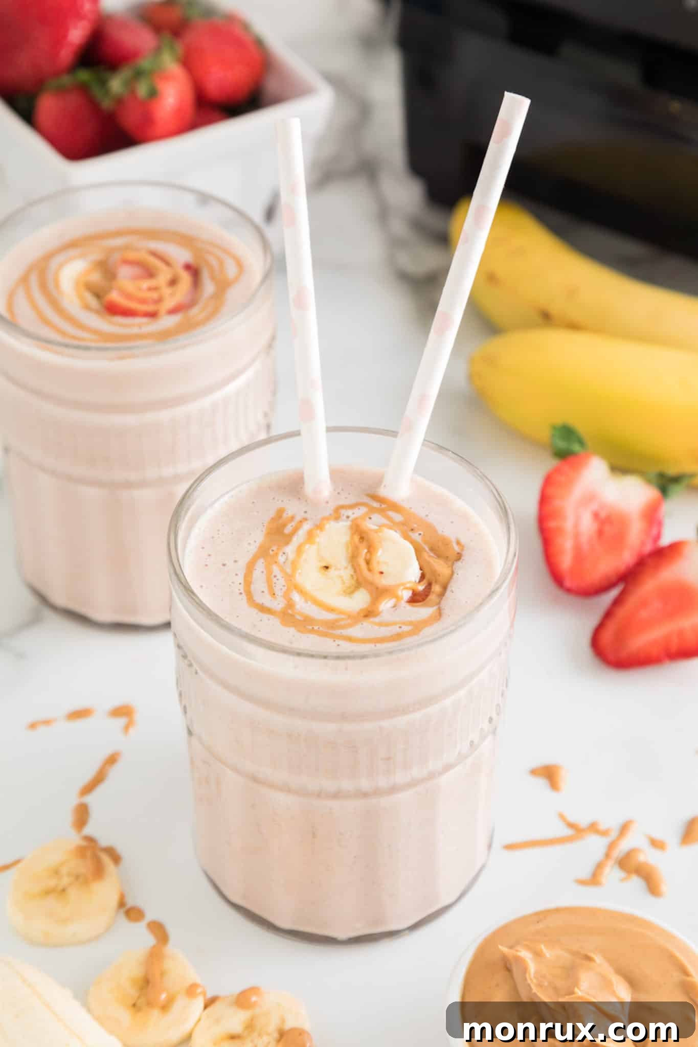 Strawberry Banana smoothie in a glass with two straws and peanut butter drizzled on top.