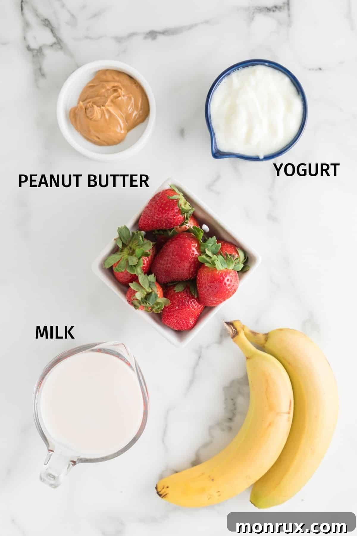 Ingredients for a strawberry banana peanut butter smoothie in small bowls on a white surface.