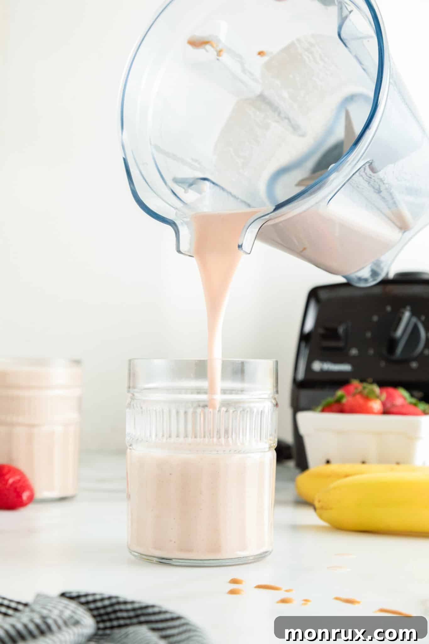 A blender jar pouring a strawberry banana PB smoothie into a glass.