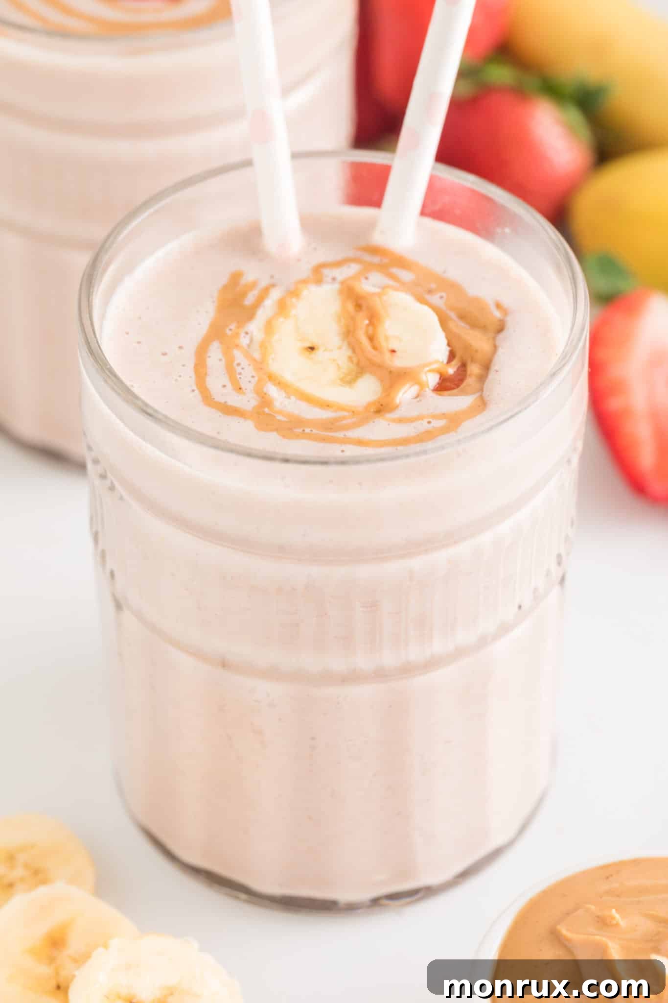 Strawberry Banana smoothie in a glass with two straws and peanut butter drizzled on top.