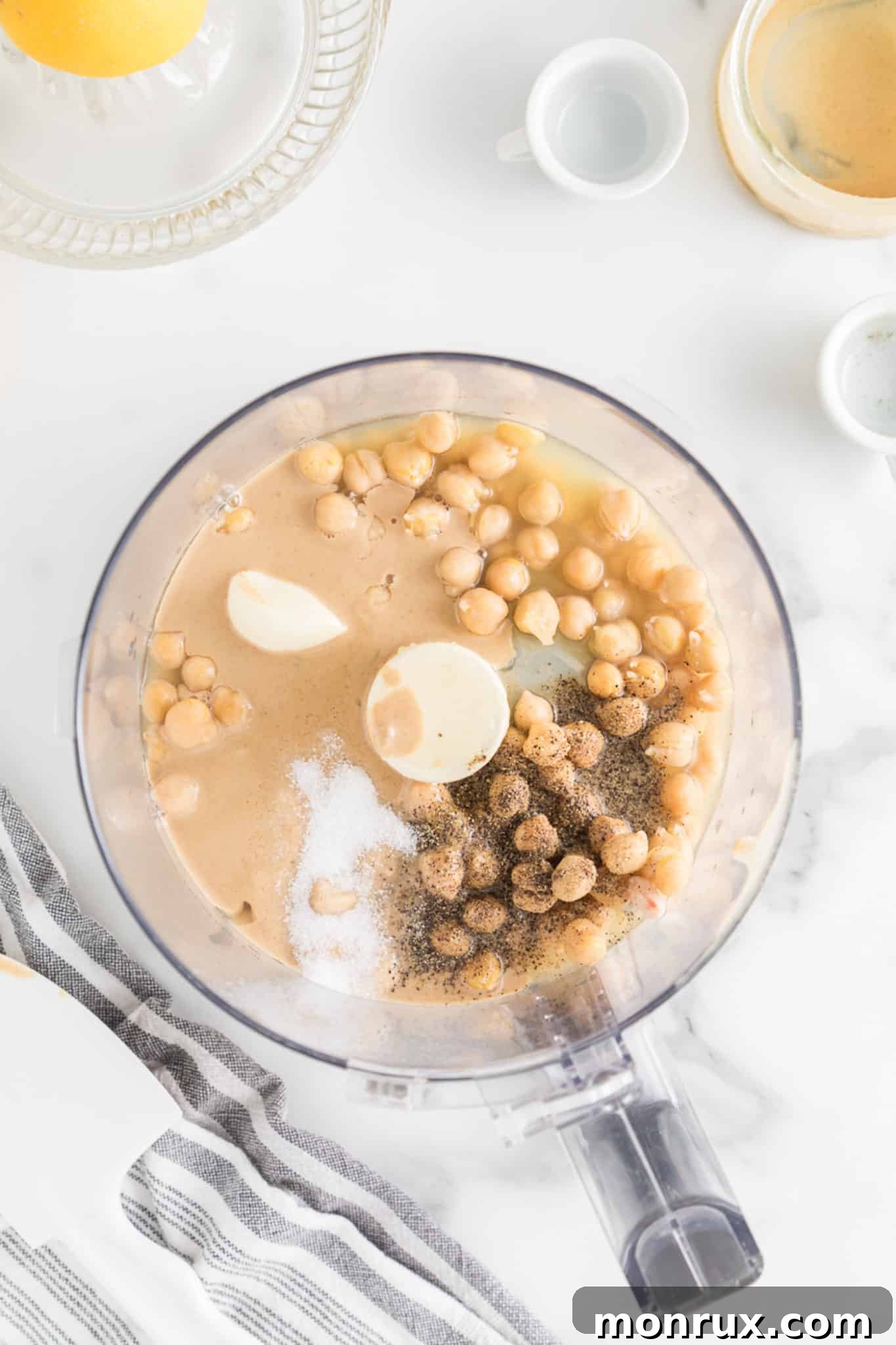 All the key ingredients for homemade hummus – chickpeas, lemon juice, tahini, and garlic – collected together in the bowl of a food processor, ready for blending.