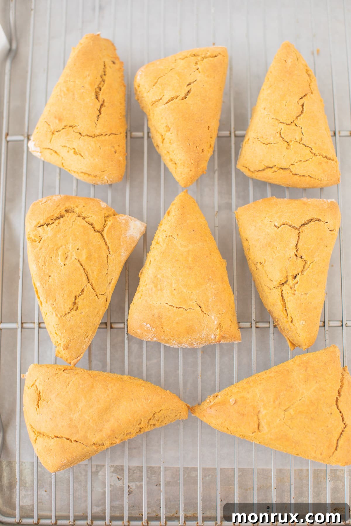 Freshly baked pumpkin scones cooling on a wire rack, their golden tops visible.