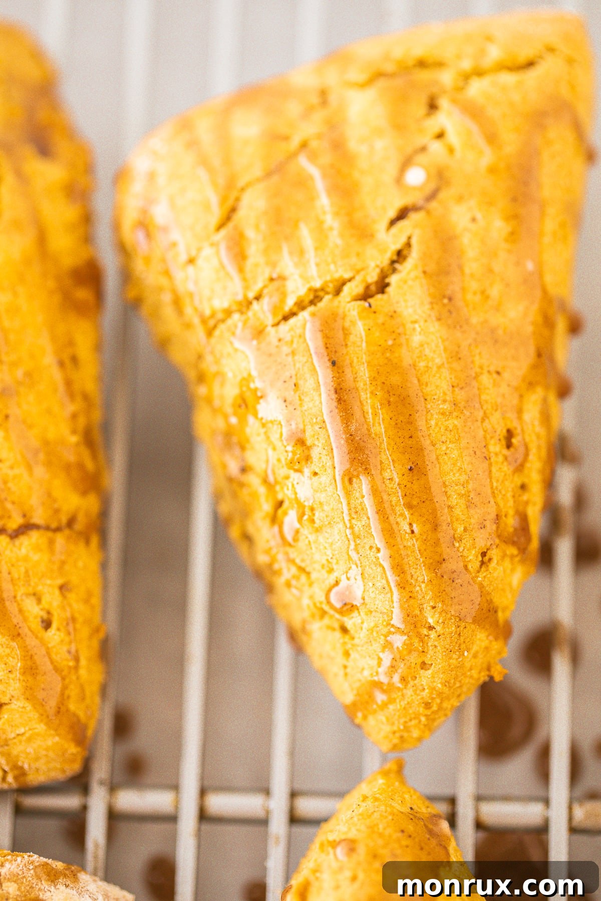 A baked pumpkin scone receiving a delicate drizzle of spiced glaze, enhancing its appeal.