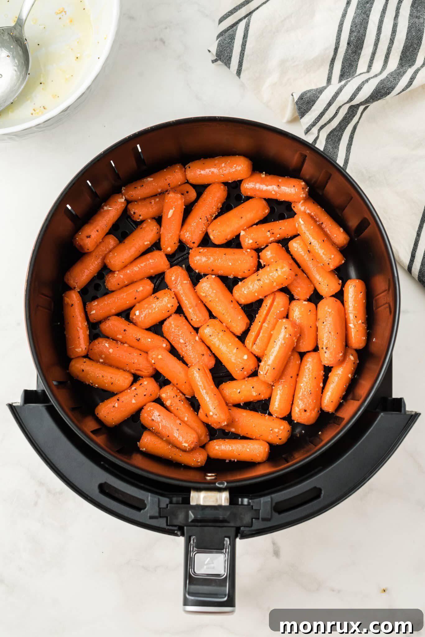 Seasoned baby carrots arranged in a single layer in the air fryer basket, ready to be cooked.