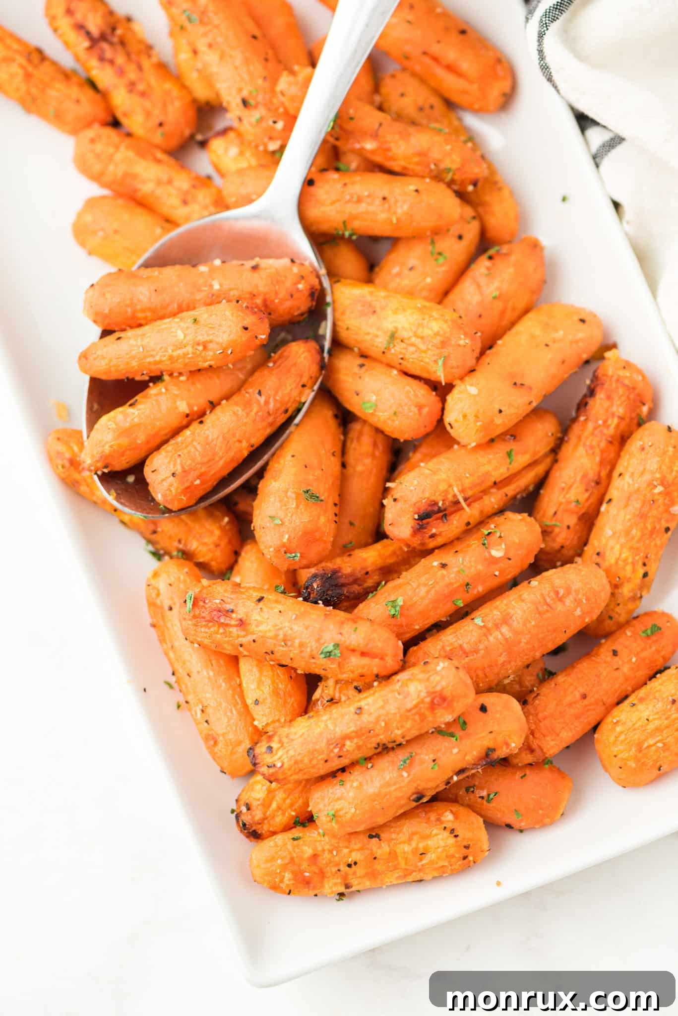 A serving plate filled with perfectly cooked air fryer baby carrots, accompanied by a spoon.