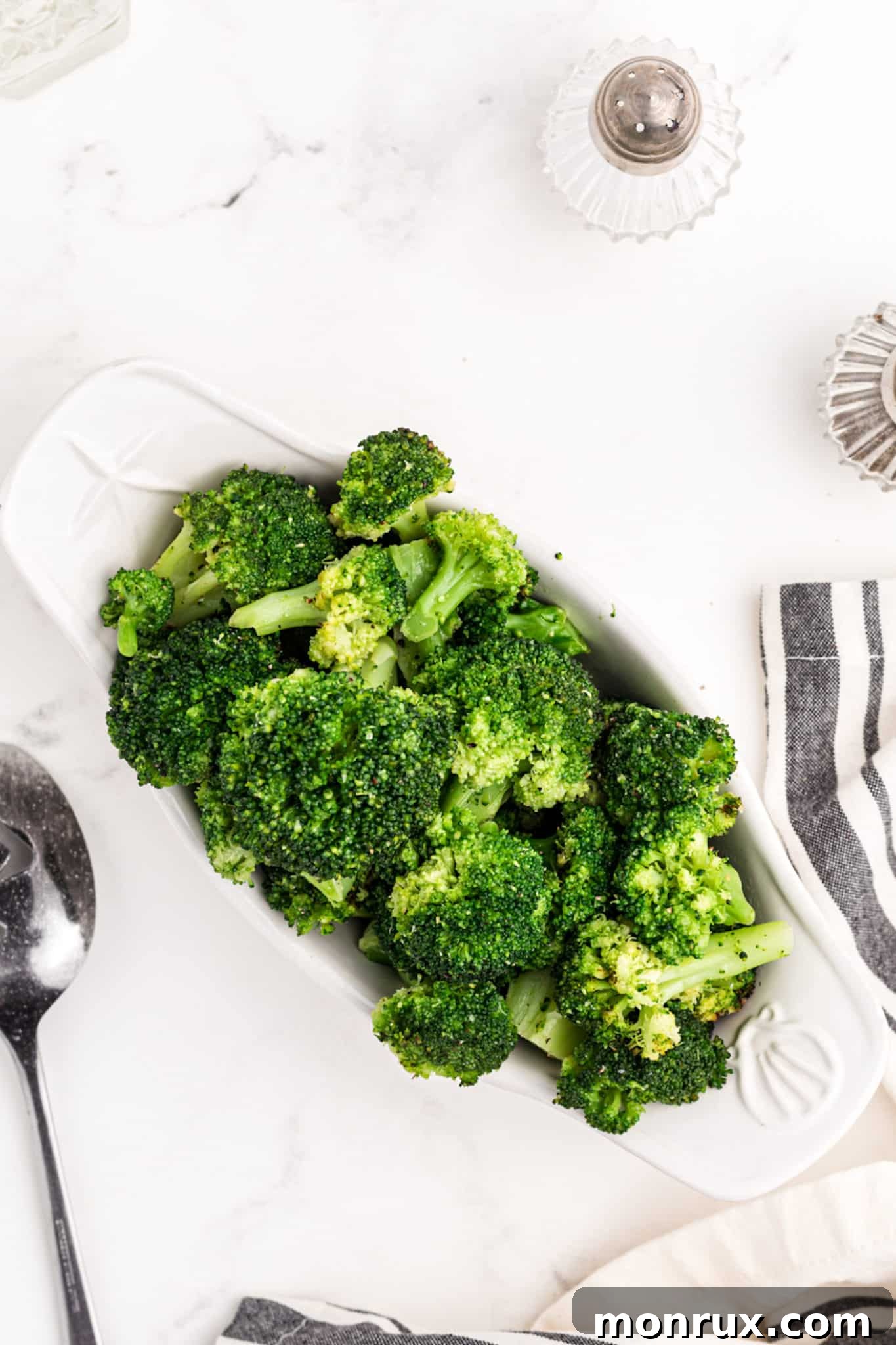 A bowl of cooked broccoli on a rustic wooden table, with salt and pepper shakers in the background.