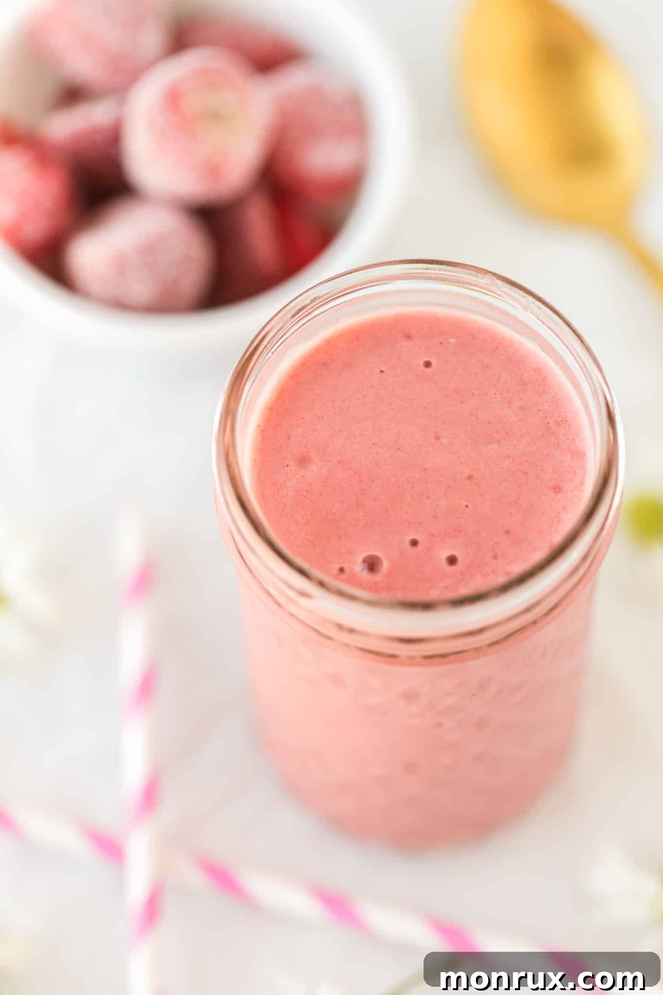 A refreshing glass of vegan strawberry milkshake with two pink striped straws, beautifully presented on a rustic wooden table, suggesting a healthy and delicious treat.