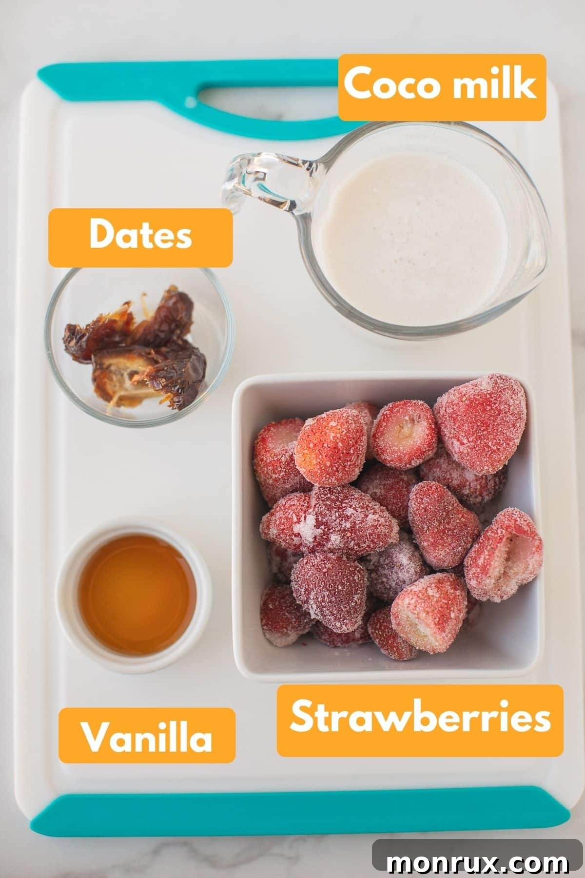 A well-organized photo of ingredients for a vegan strawberry smoothie, featuring frozen strawberries, plump dates, a bottle of vanilla extract, and a can of coconut milk, clearly laid out.
