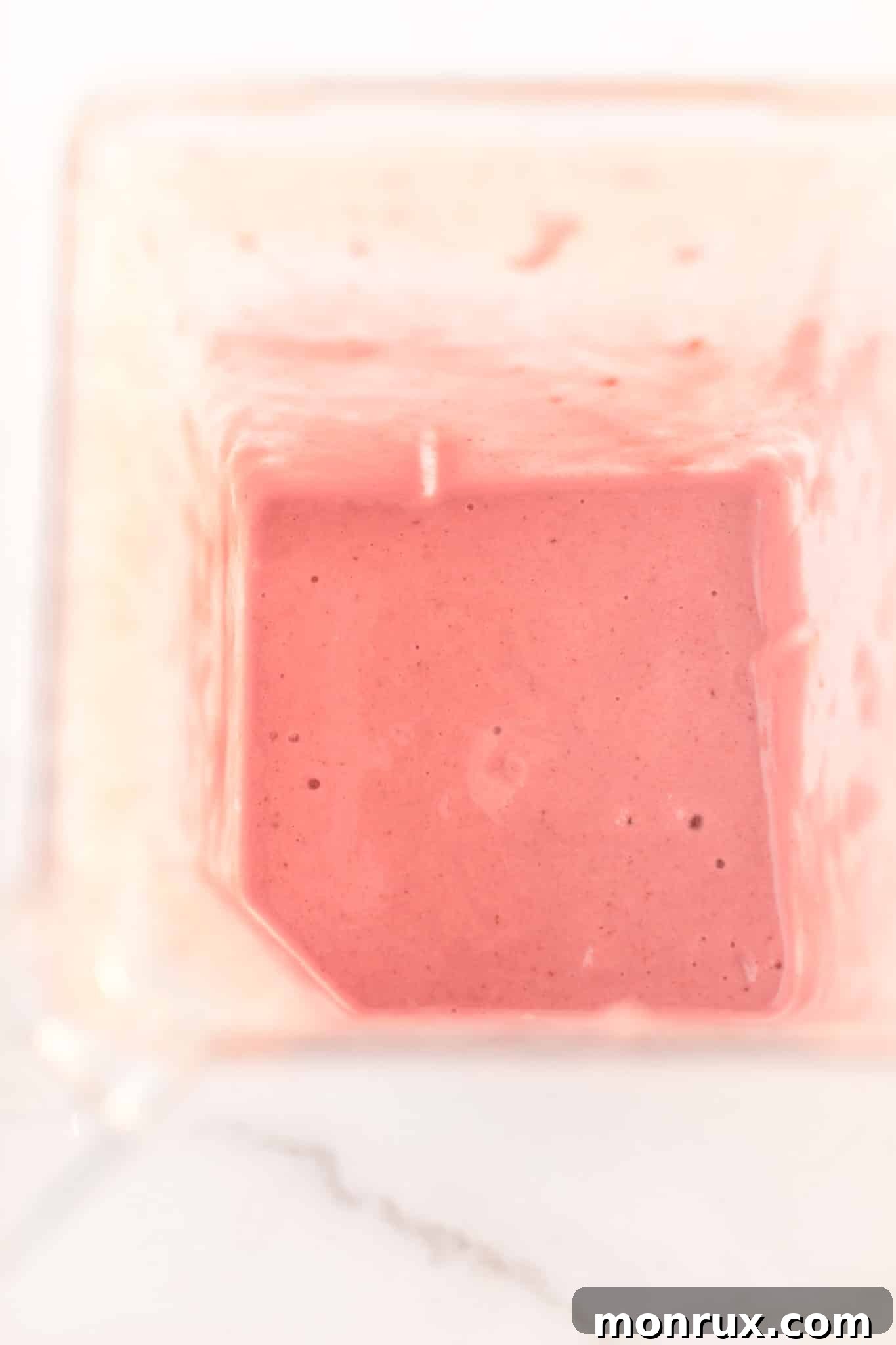 A perfectly blended strawberry milkshake, showcasing its smooth and inviting texture, still in the blender and ready to be poured into glasses.