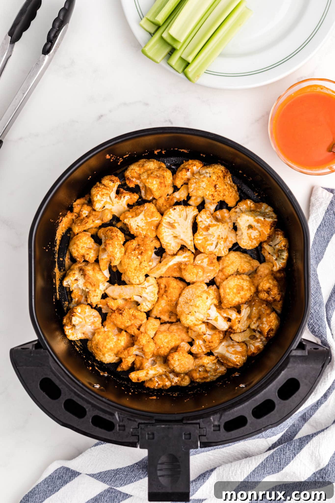 Golden-brown cauliflower florets cooking evenly in an air fryer basket, showing their crispy texture before being tossed in sauce.