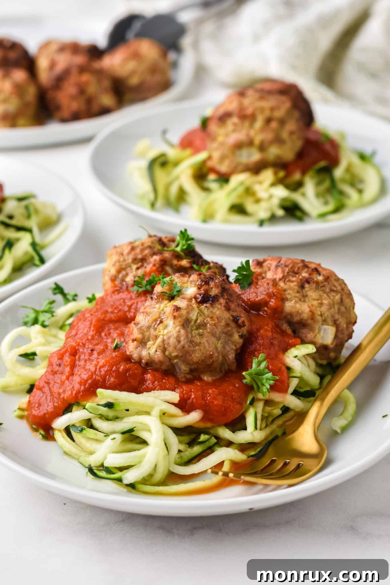 Three plates of zoodles topped with red sauce and air fried turkey meatballs, garnished with fresh parsley.
