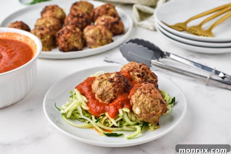 A plate of zoodles and turkey meatballs with serving dishes in the background, ready for a healthy meal.