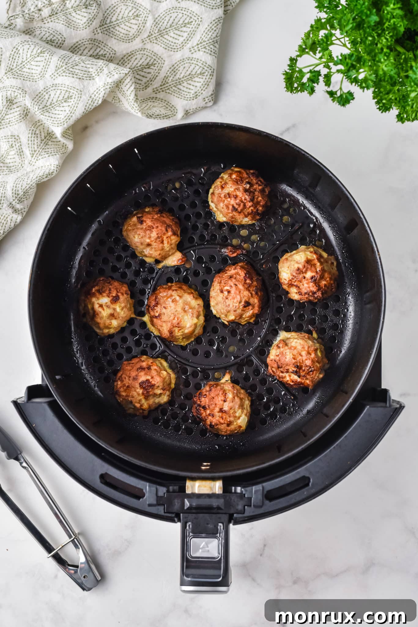 Turkey meatballs cooking in the basket of an air fryer, golden brown and perfectly cooked.