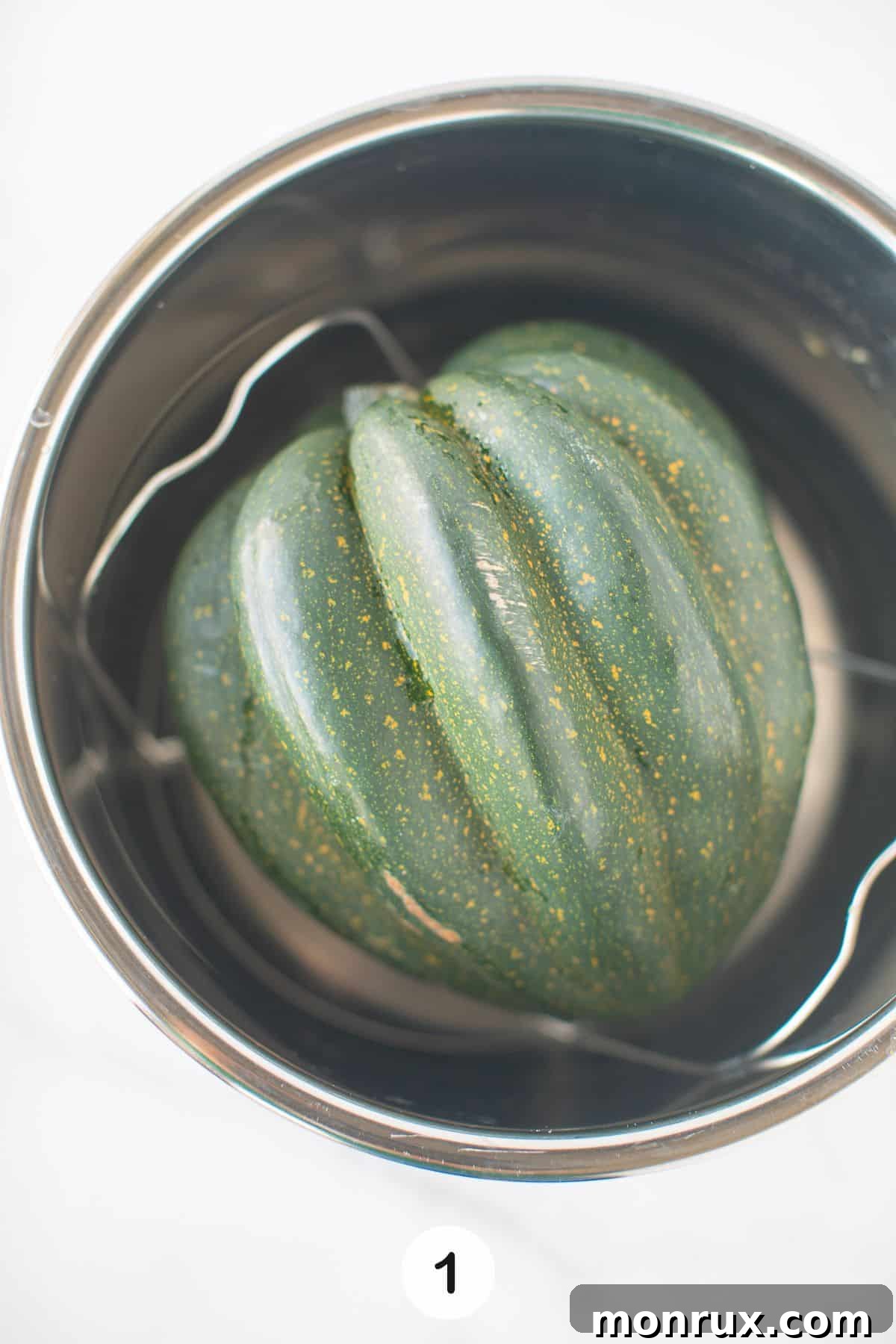 A whole, uncooked acorn squash being placed into an Instant Pot steamer basket.